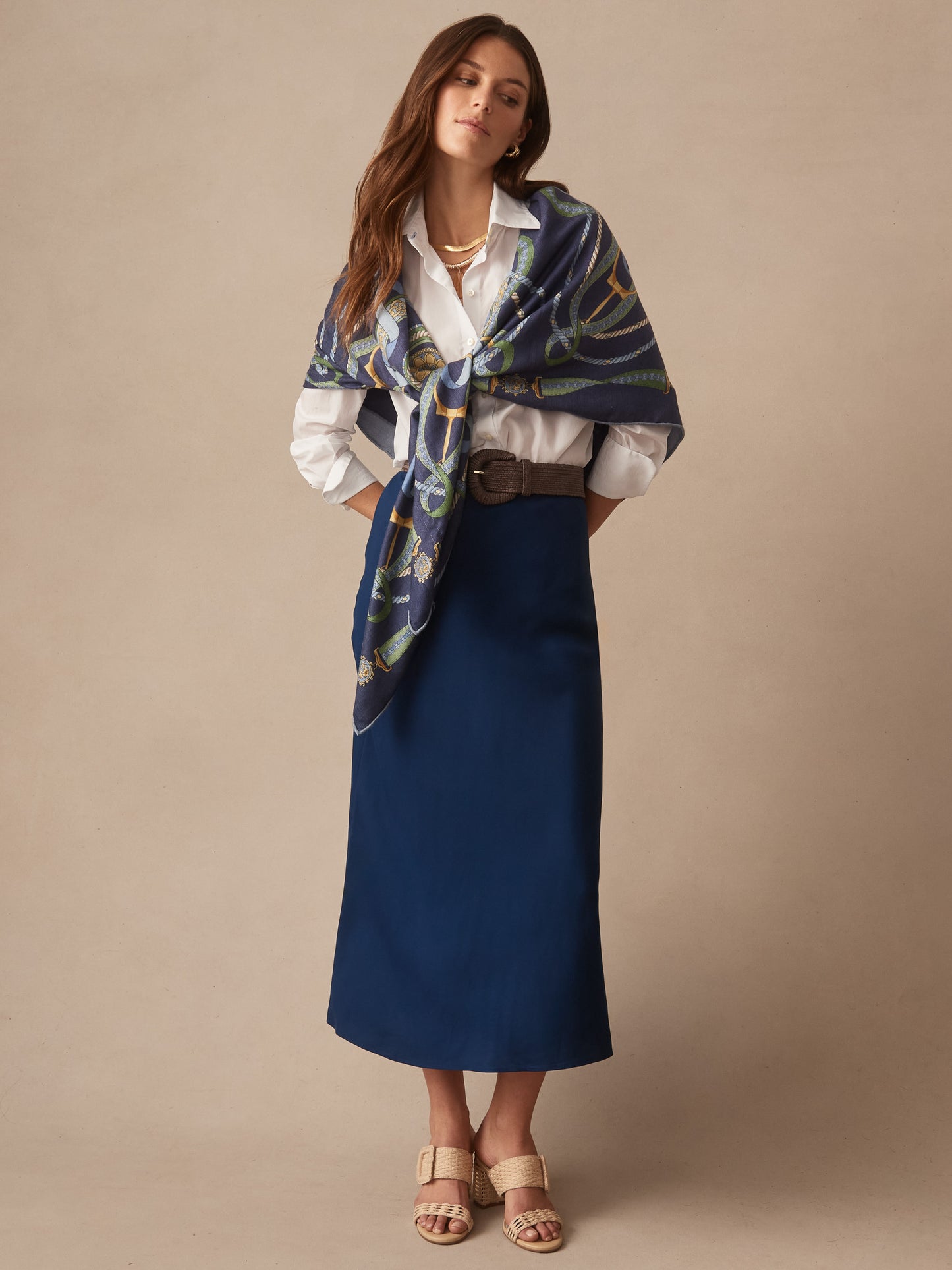 Woman wearing a navy Adelyn Skirt styled with a white shirt, woven belt, and patterned scarf by J.McLaughlin, showcasing effortlessly stylish, enduring designs and innovative fabrics.