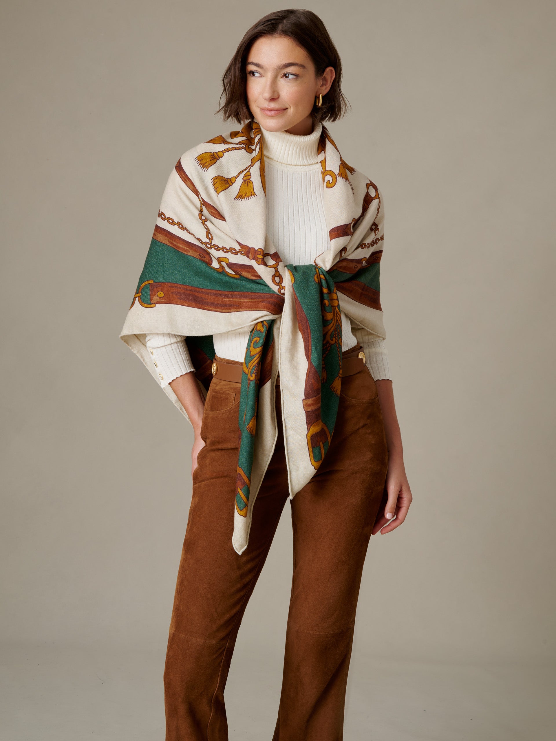 The Charlotte Scarf in Gilded Bridle Border by J.McLaughlin draped over a white sweater with a bold equestrian border and warm brown trousers.