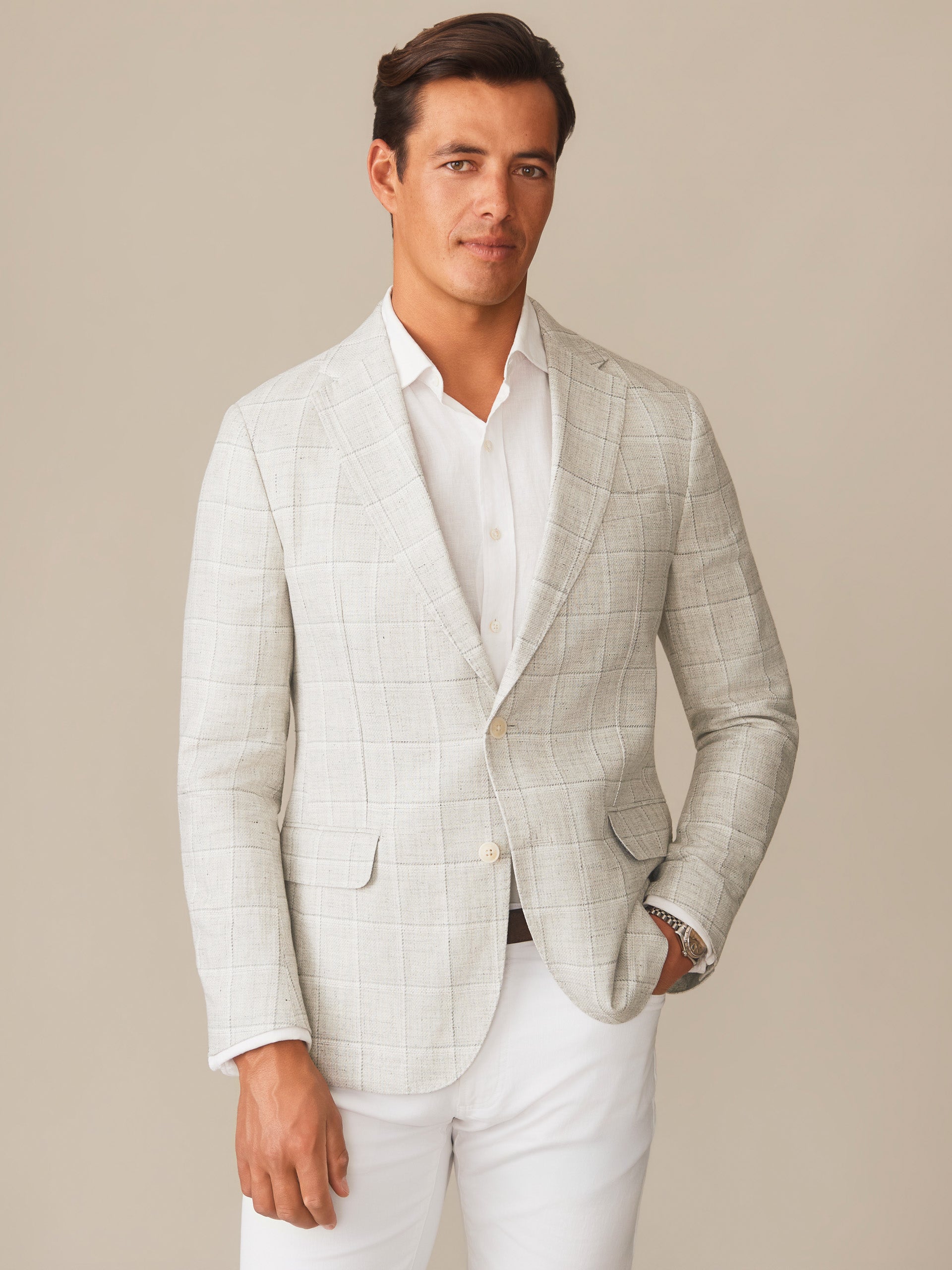 A male model wears the Suffolk Linen Sport Coat in Window Pane by J. McLaughlin, showcasing effortlessly stylish tailoring in light gray linen with classic windowpane pattern, reflecting enduring designs and innovative fabrics from a destination for defining style. Life, Well-Lived.