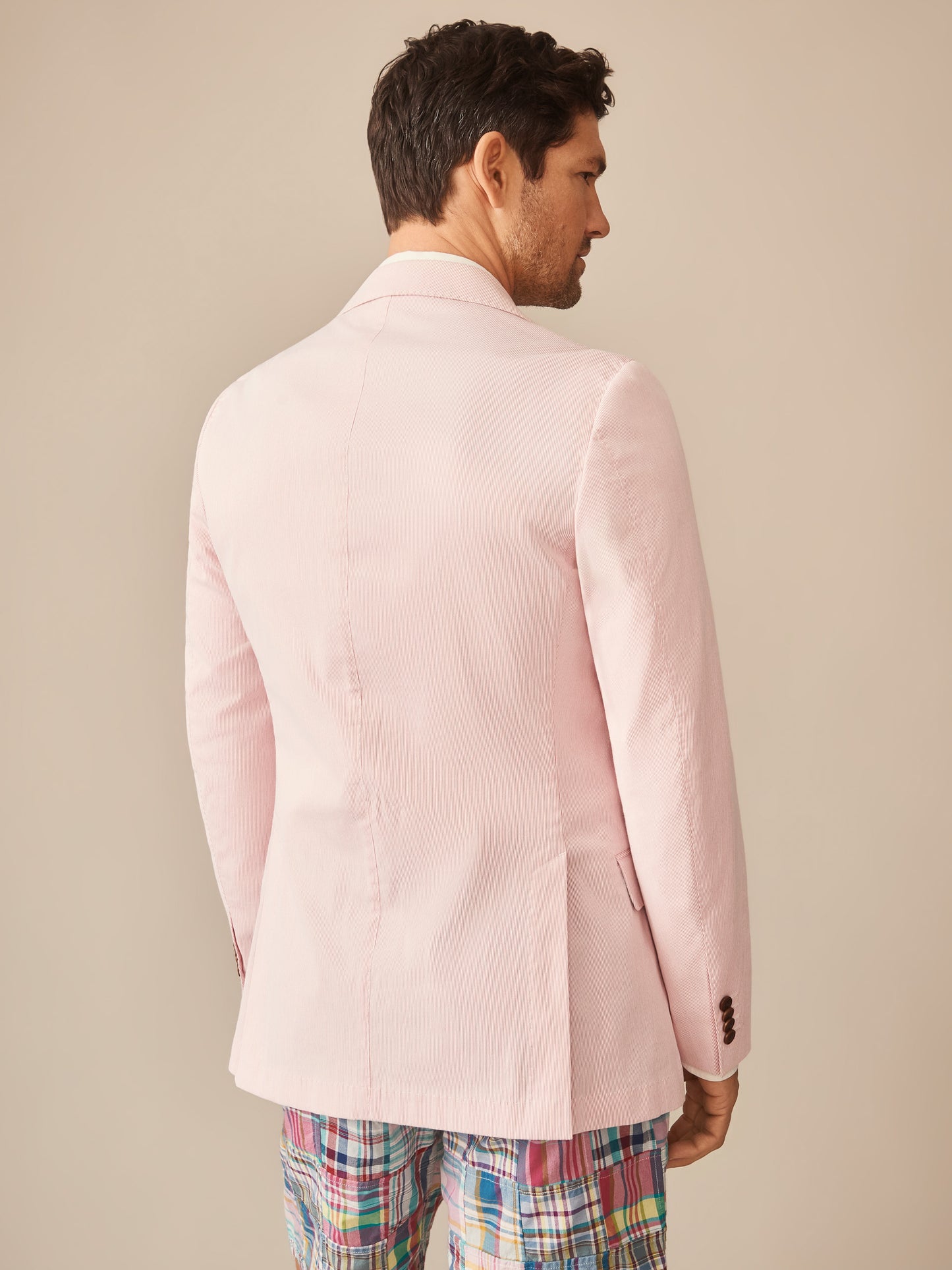 Man wearing a pale pink Suffolk Sport Coat in Fineline by J.McLaughlin, paired with colorful plaid pants, showcasing effortlessly stylish and enduring designs with innovative fabrics.