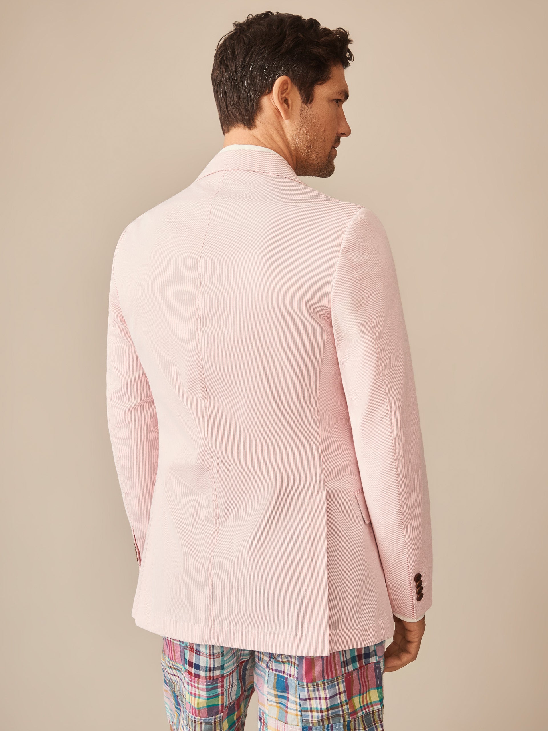 Man wearing a pale pink Suffolk Sport Coat in Fineline by J.McLaughlin, paired with colorful plaid pants, showcasing effortlessly stylish and enduring designs with innovative fabrics.