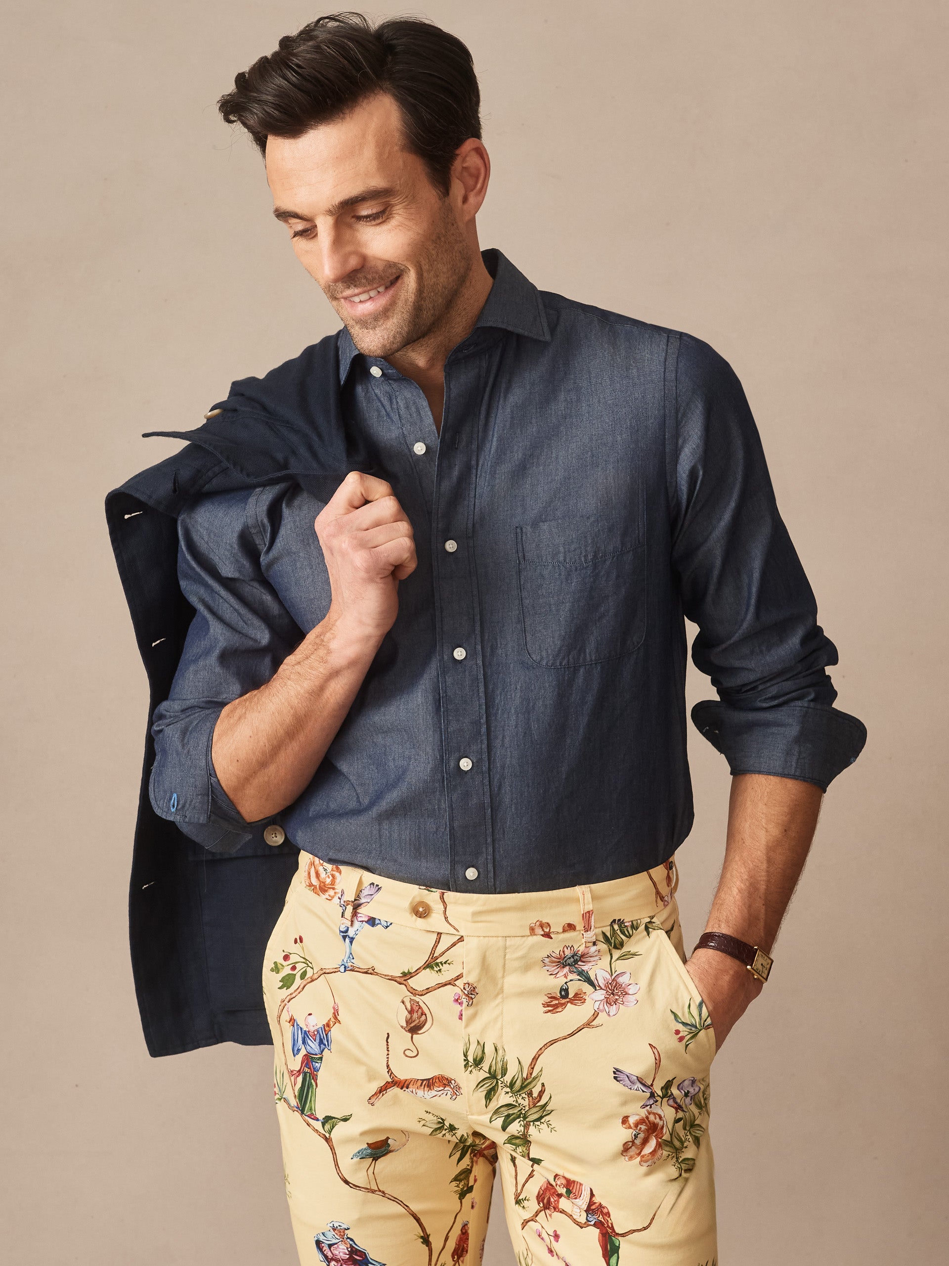 Man wearing a navy Gramercy Cotton Chambray Shirt by J.McLaughlin paired with floral patterned pants, showcasing effortlessly stylish, enduring designs in innovative fabrics, a destination for defining style. Life, Well-Lived.