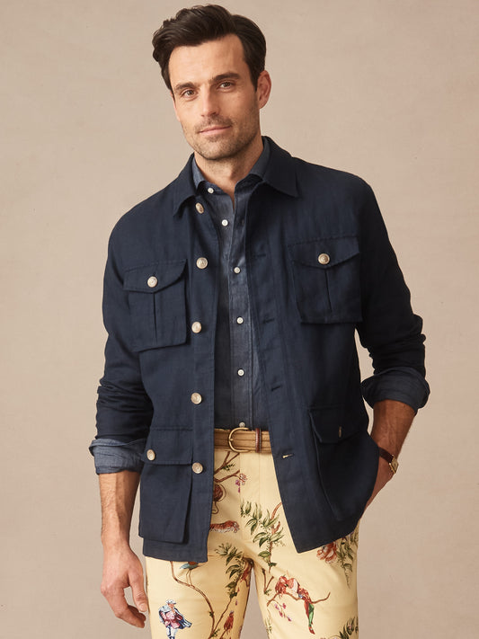 Man wearing a navy Aston Linen Safari Jacket by J.McLaughlin over a chambray shirt and patterned cream trousers, showcasing effortlessly stylish, enduring designs with innovative fabrics.