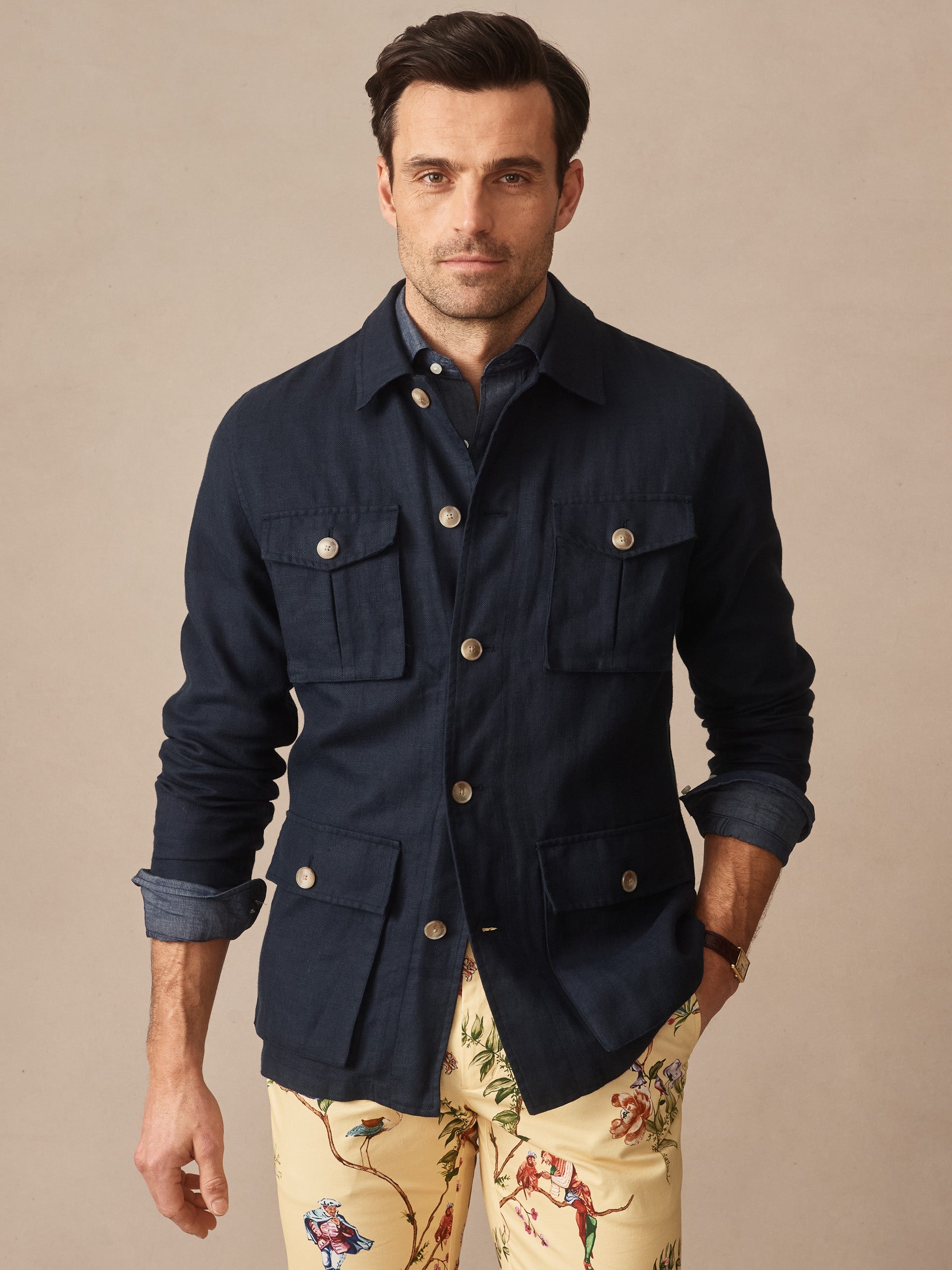 Man wearing a navy Aston Linen Safari Jacket by J.McLaughlin, styled with rolled sleeves and paired with patterned pants, showcasing effortlessly stylish, enduring designs and innovative fabrics.