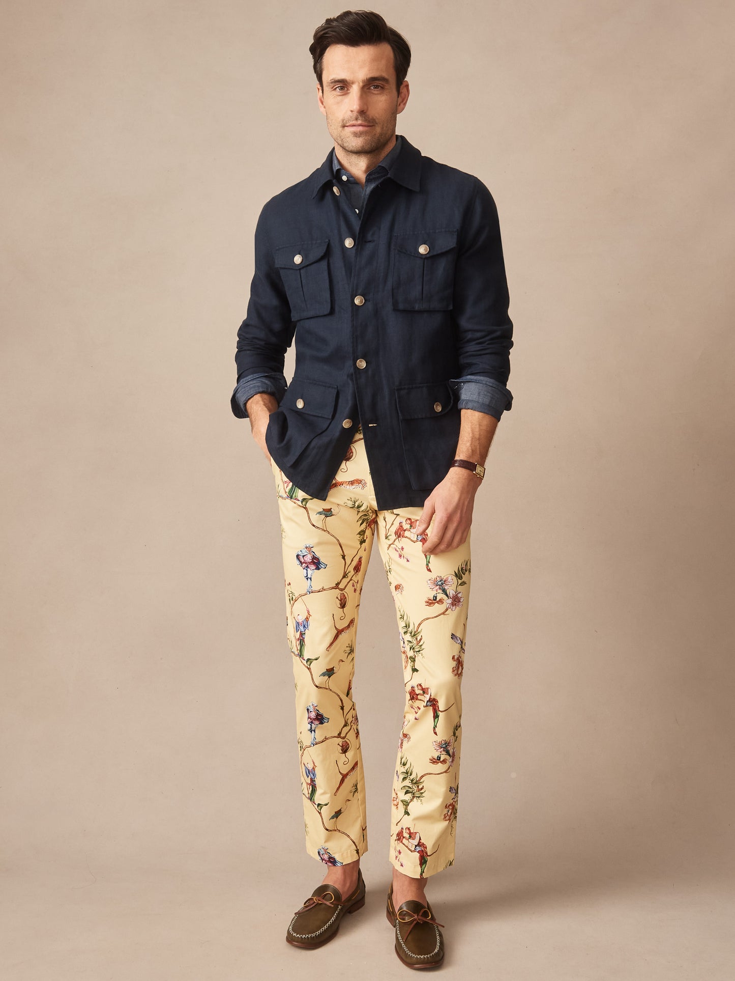 Man wearing a navy Aston Linen Safari Jacket by J.McLaughlin paired with floral patterned pants and brown loafers, showcasing effortlessly stylish, enduring designs and innovative fabrics.
