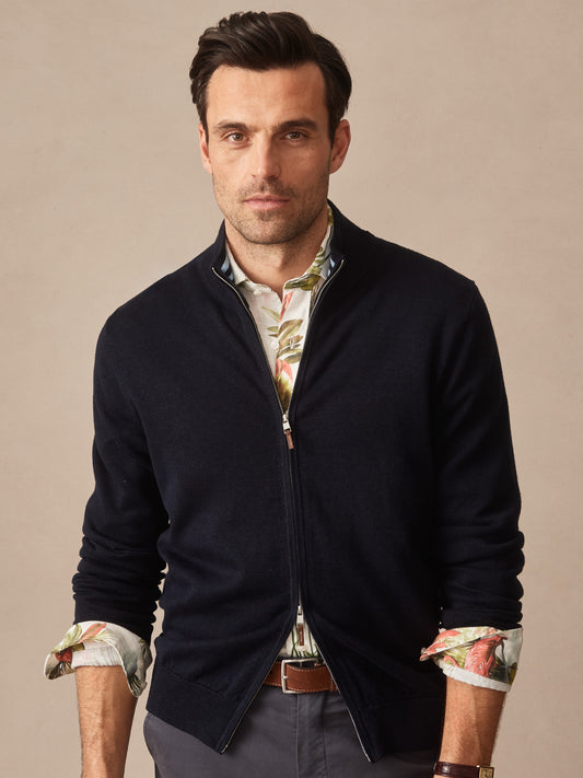 Man wearing a dark washed black Orwell Sweater by J.McLaughlin over a floral shirt, showcasing effortlessly stylish layering with enduring designs and innovative fabrics. A destination for defining style. Life, Well-Lived.