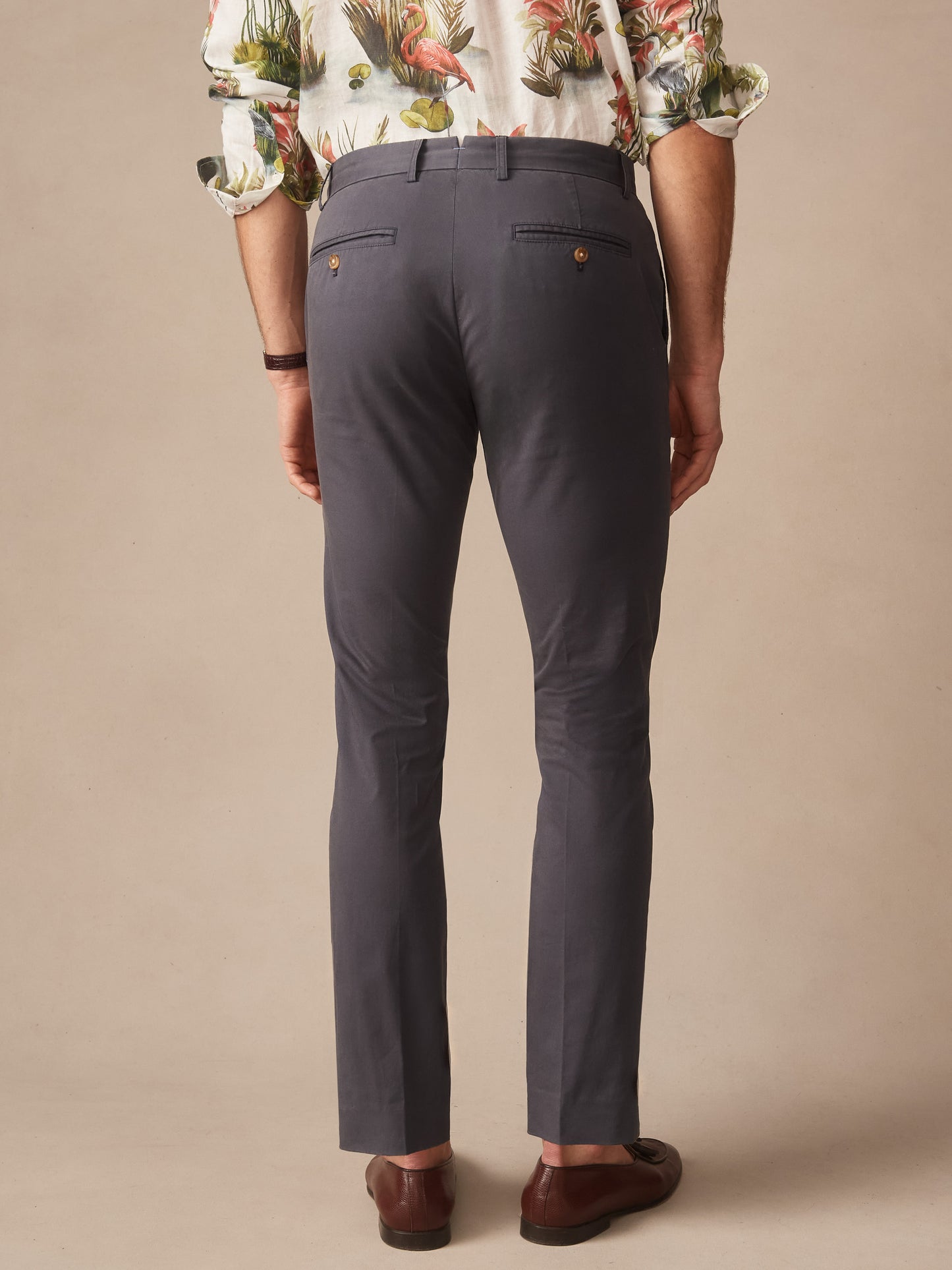 Back view of a man wearing J.McLaughlin Madison Pants in washed black, paired with brown leather shoes and a tropical print shirt, showcasing effortlessly stylish and enduring designs for a life well-lived.