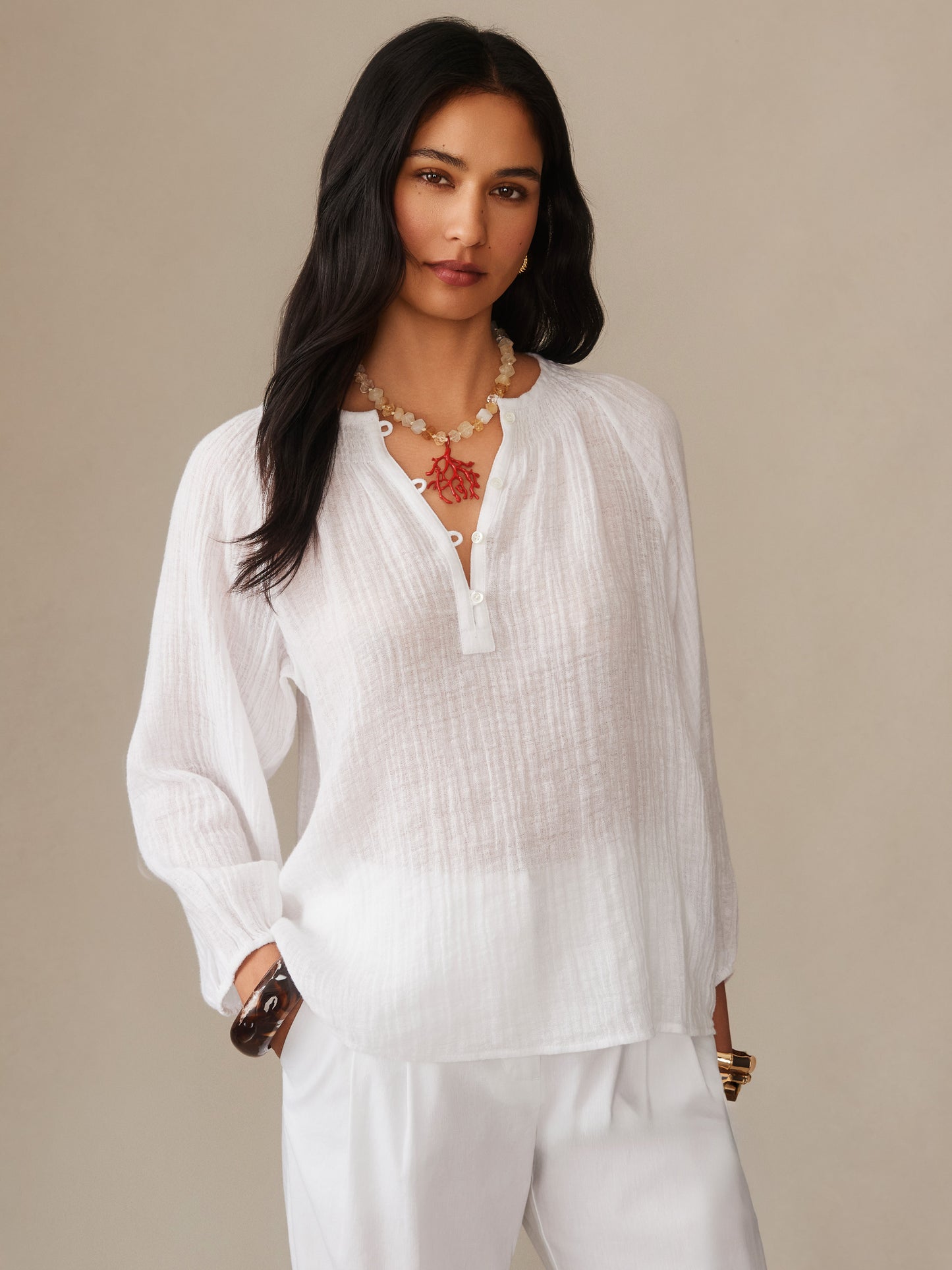 Woman wearing a white Tatiana Linen Blouse by J.McLaughlin, styled with white pants and layered necklaces, embodying effortlessly stylish, enduring designs and innovative fabrics.
