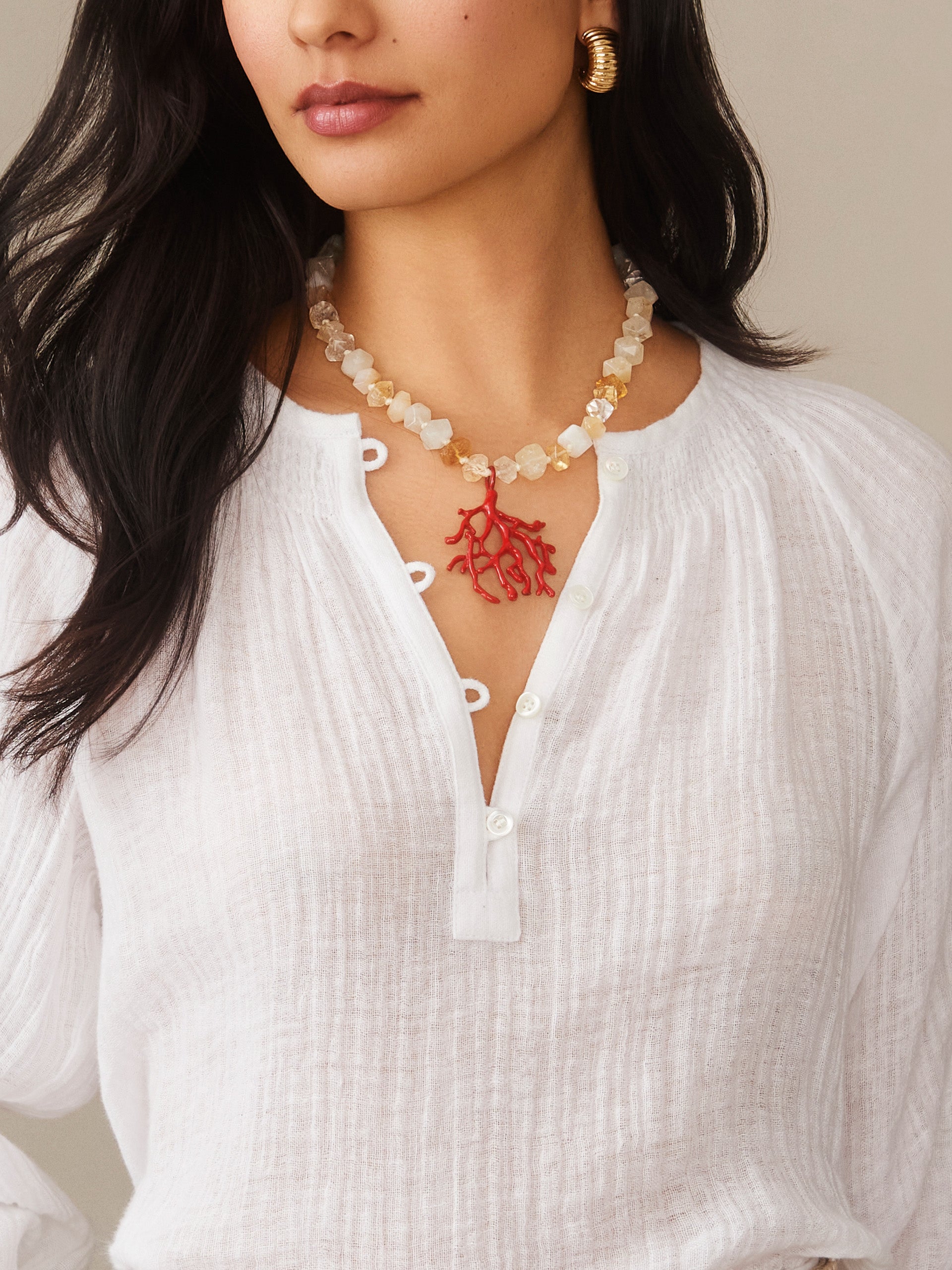 Close-up of a woman wearing a Coral Necklace by J.McLaughlin featuring translucent beads and a vibrant coral-inspired pendant, paired with a white textured blouse, showcasing effortlessly stylish, enduring designs from a destination for defining style. Life, Well-Lived.