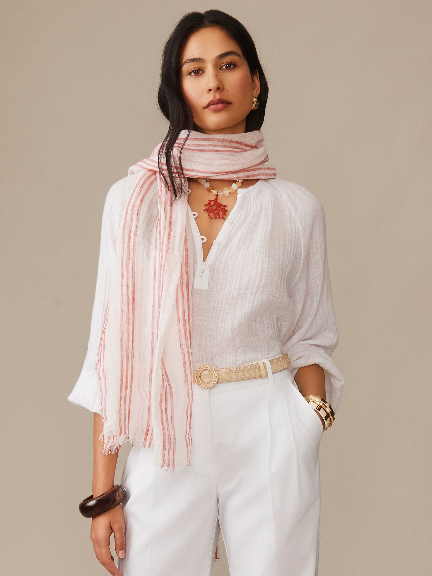 Woman wearing a J.McLaughlin Tessa Linen Scarf in Stripe in soft pink paired with a white blouse and pants, showcasing effortlessly stylish, enduring designs and innovative fabrics.