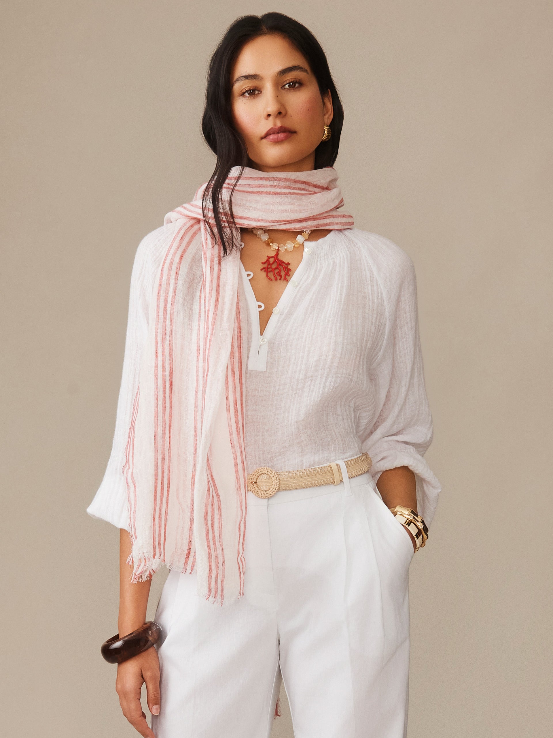 Woman wearing a J.McLaughlin Tessa Linen Scarf in Stripe in soft pink paired with a white blouse and pants, showcasing effortlessly stylish, enduring designs and innovative fabrics.