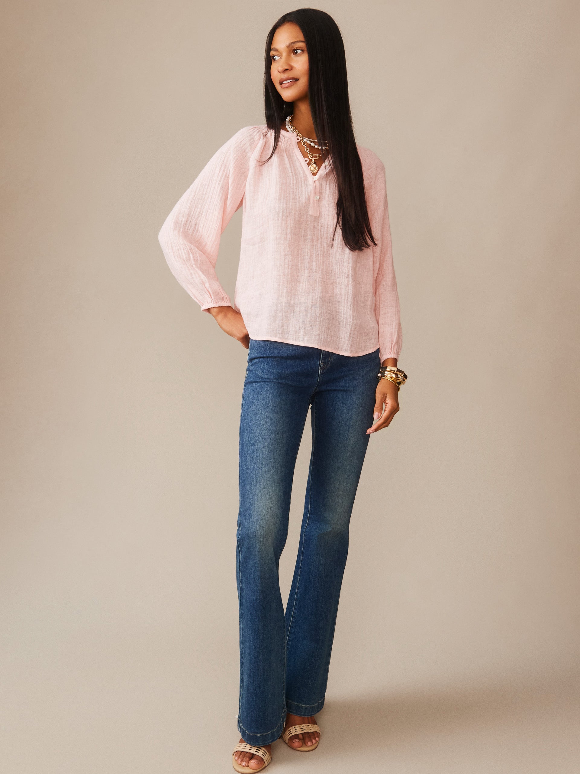 Woman wearing a pink Tatiana Linen Blouse by J.McLaughlin paired with blue jeans and sandals, showcasing effortlessly stylish, enduring designs with a legacy of timeless fashion.