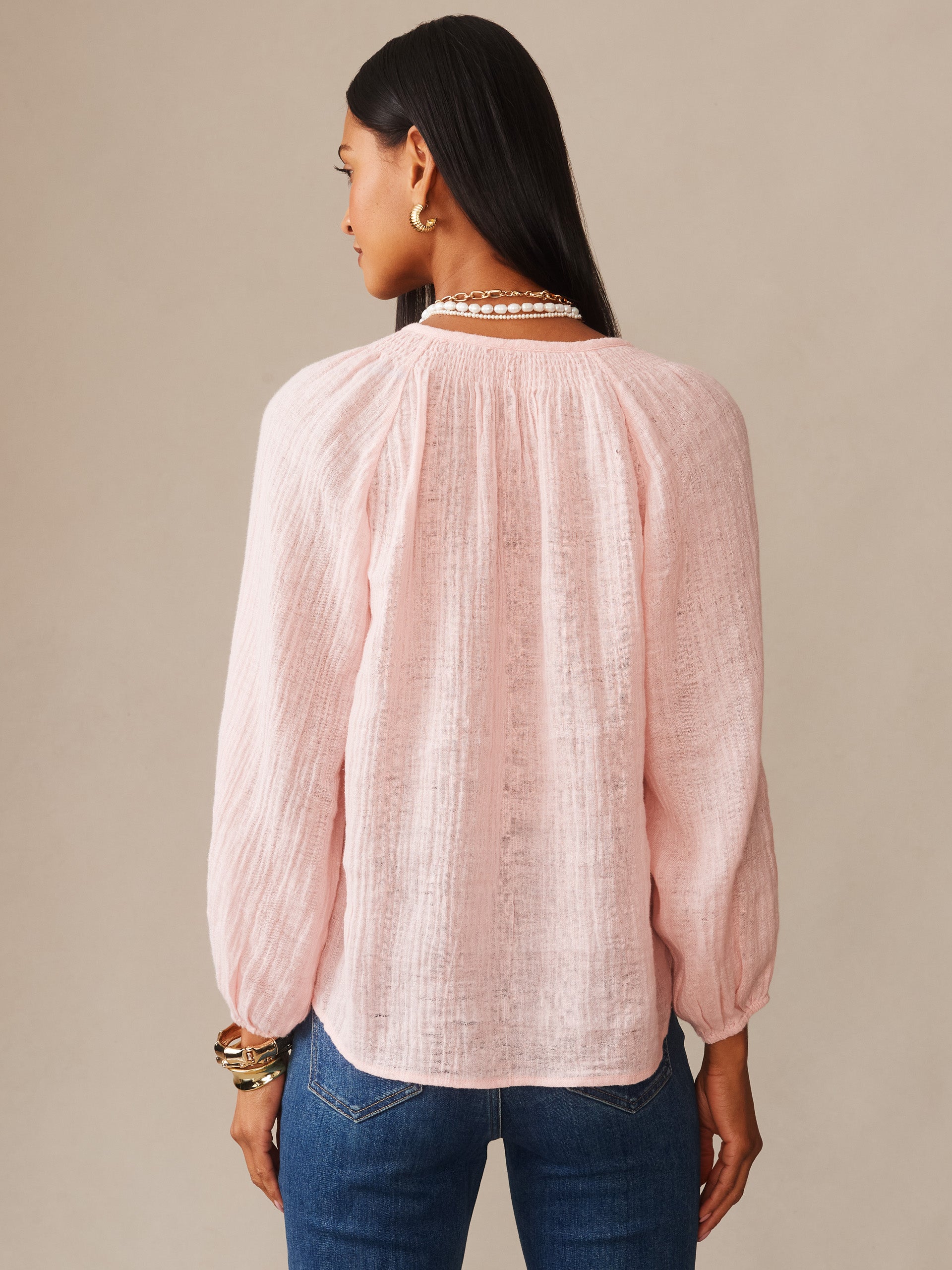 Woman wearing a soft pink Tatiana Linen Blouse by J.McLaughlin, styled with pearl necklace and gold earrings, showcasing effortlessly stylish, enduring designs.