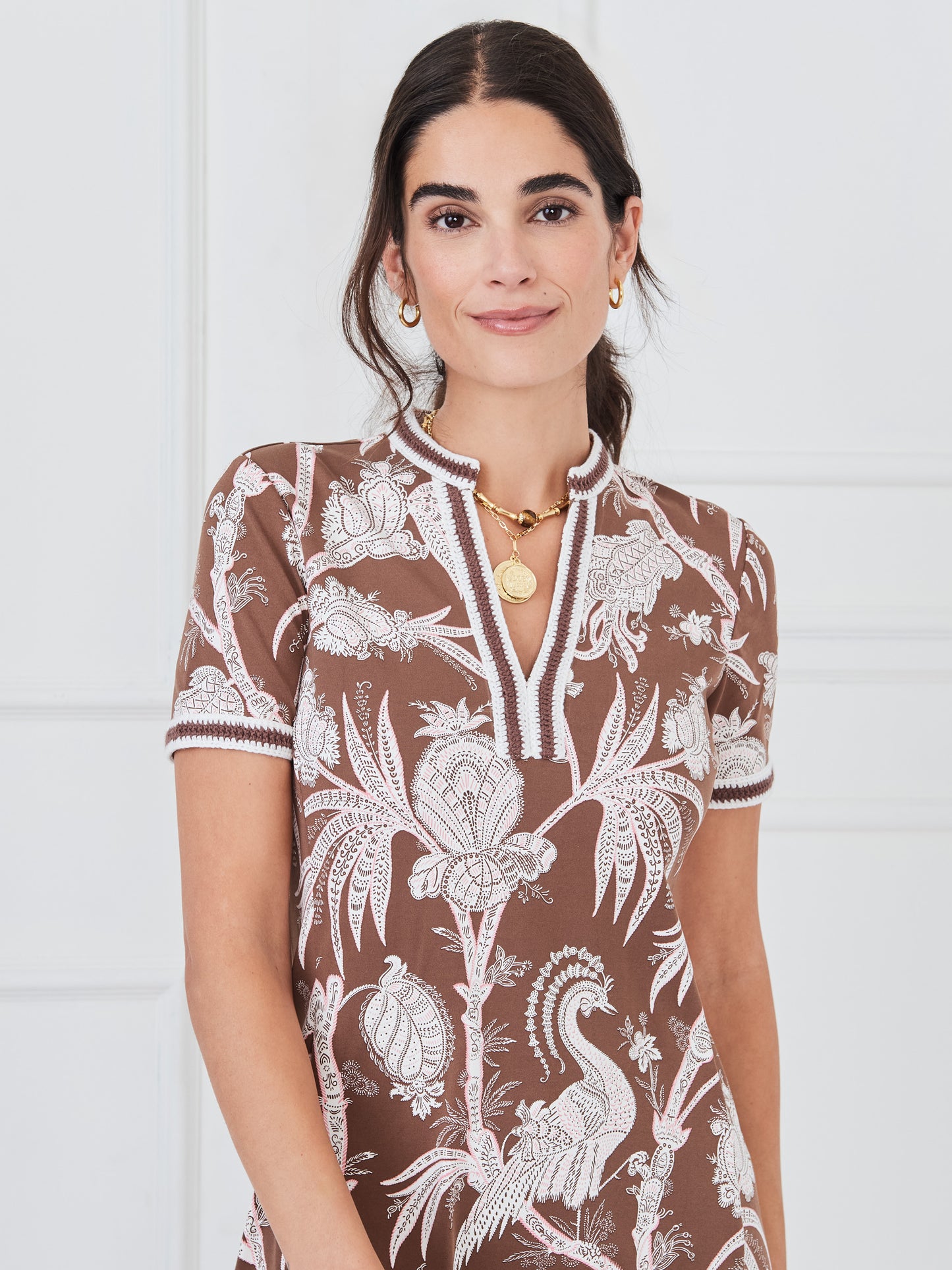 Woman wearing a J.McLaughlin Tesni Dress in Pomegrante Meadow featuring a brown base with white intricate floral and bird patterns, short sleeves, and a v-neckline.