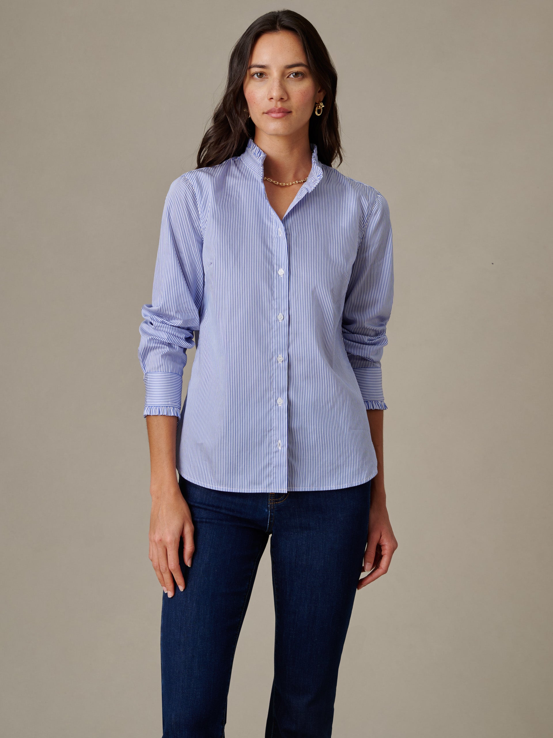 Woman wearing a classic striped blouse with ruffle collar and long sleeves, paired with dark jeans, showcasing the Tess Ruffle Collar Shirt in Stripe by J.McLaughlin.