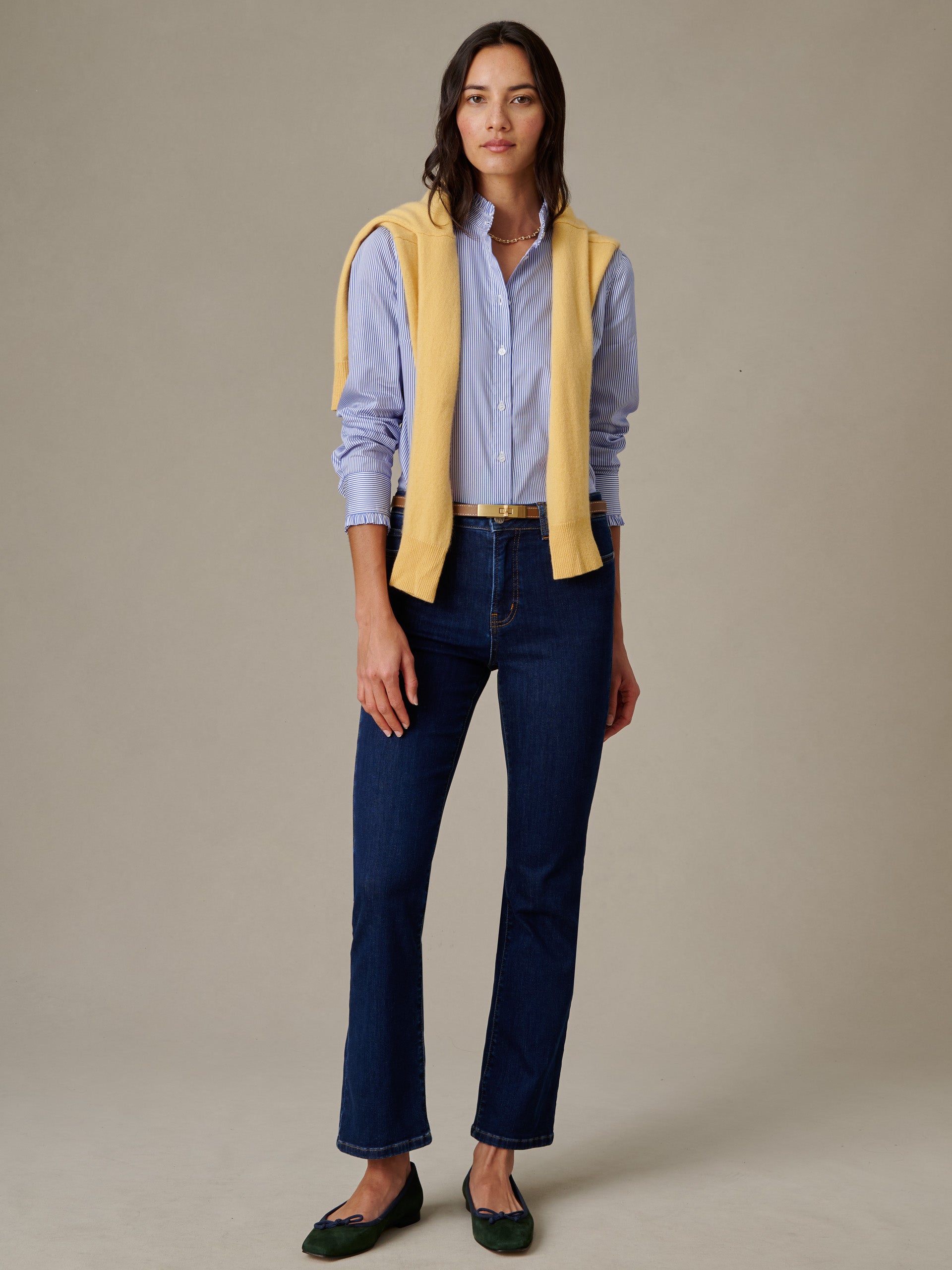 Woman wearing Tess Ruffle Collar Shirt in Stripe by J.McLaughlin paired with dark jeans and a yellow sweater draped over shoulders, embodying effortless style and timeless fashion.