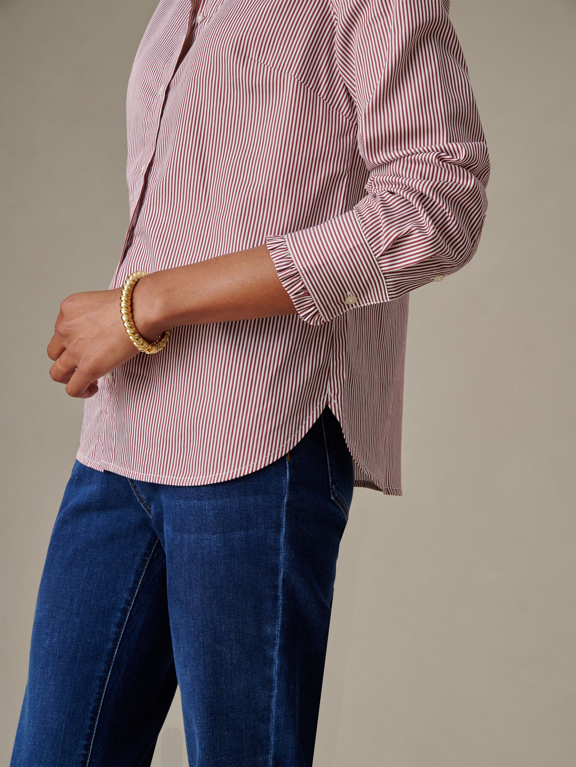 Side view of a person wearing the Tess Ruffle Collar Shirt in Stripe by J.McLaughlin, paired with blue jeans and a gold bracelet, showcasing timeless, enduring style.