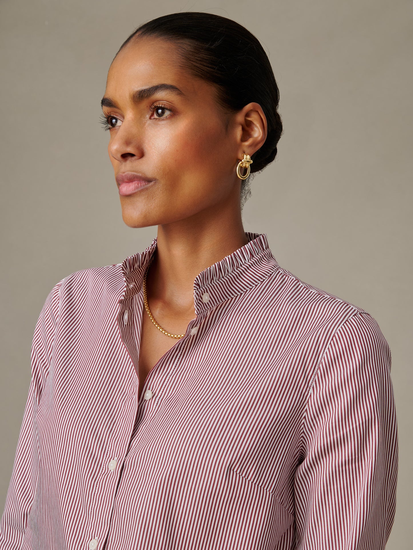 Woman wearing a striped button-up shirt with ruffle collar, featuring timeless style and impeccable craftsmanship from J.McLaughlin’s Tess Ruffle Collar Shirt in Stripe collection.