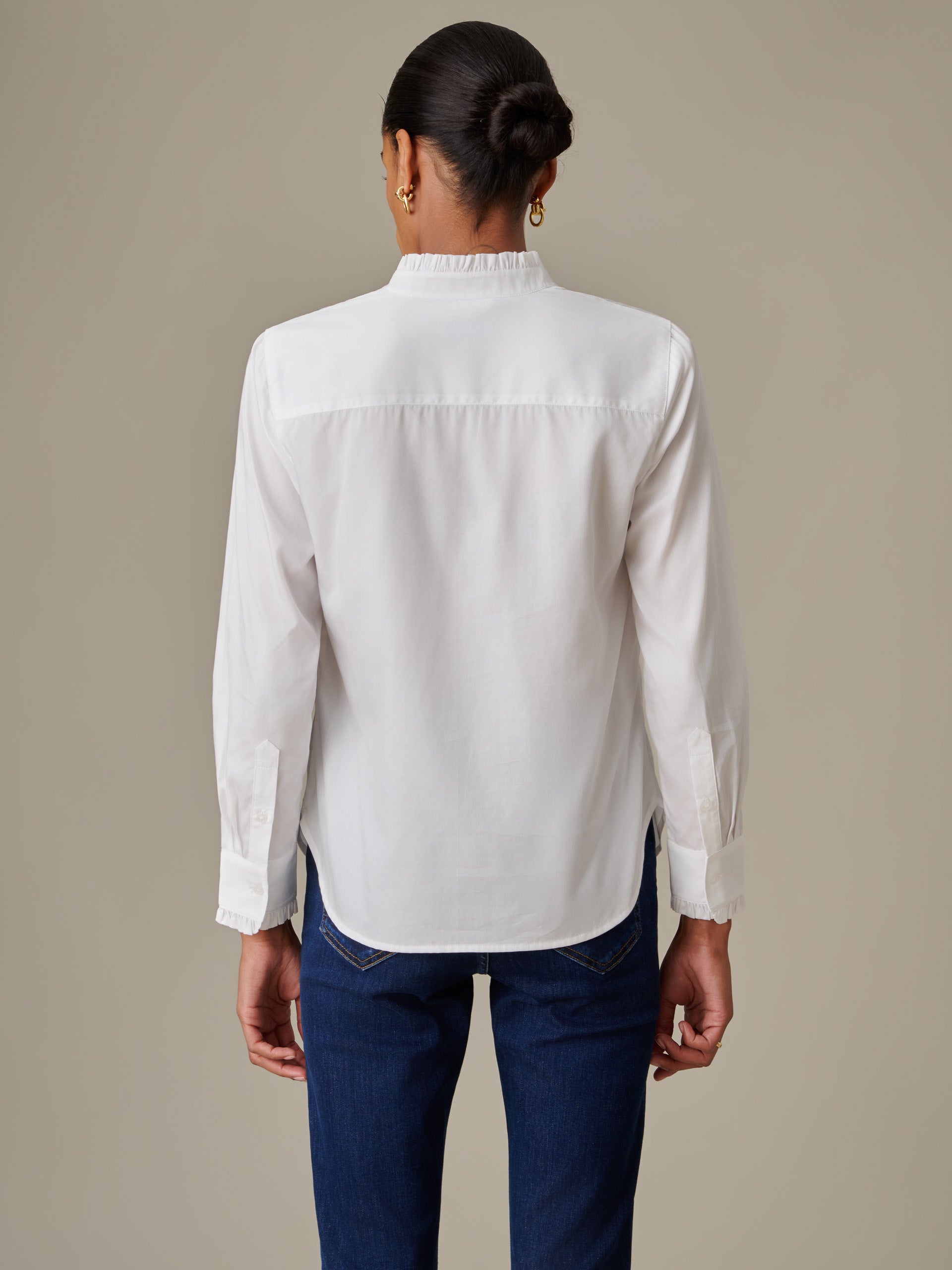Model wearing a white Tess Ruffle Collar Shirt by J.McLaughlin, showcasing the back with long sleeves and a ruffled collar, paired with dark blue jeans.