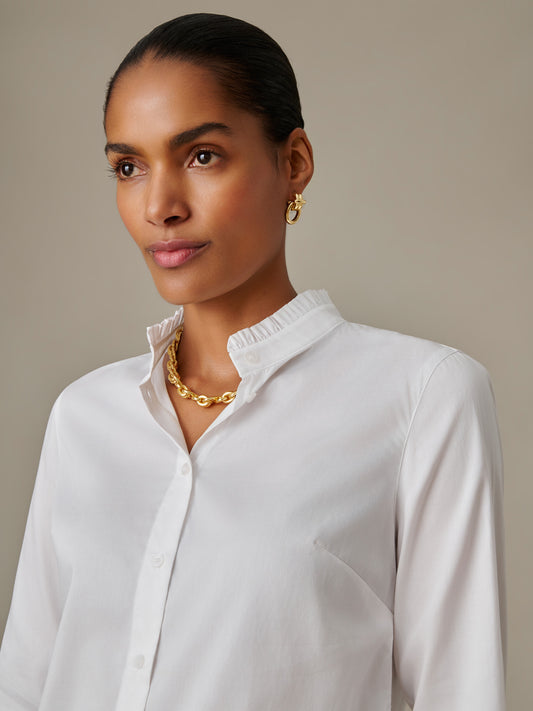 Woman wearing a white Tess Ruffle Collar Shirt by J.McLaughlin featuring a delicate ruffle collar, styled with gold jewelry, showcasing timeless elegance and enduring design.