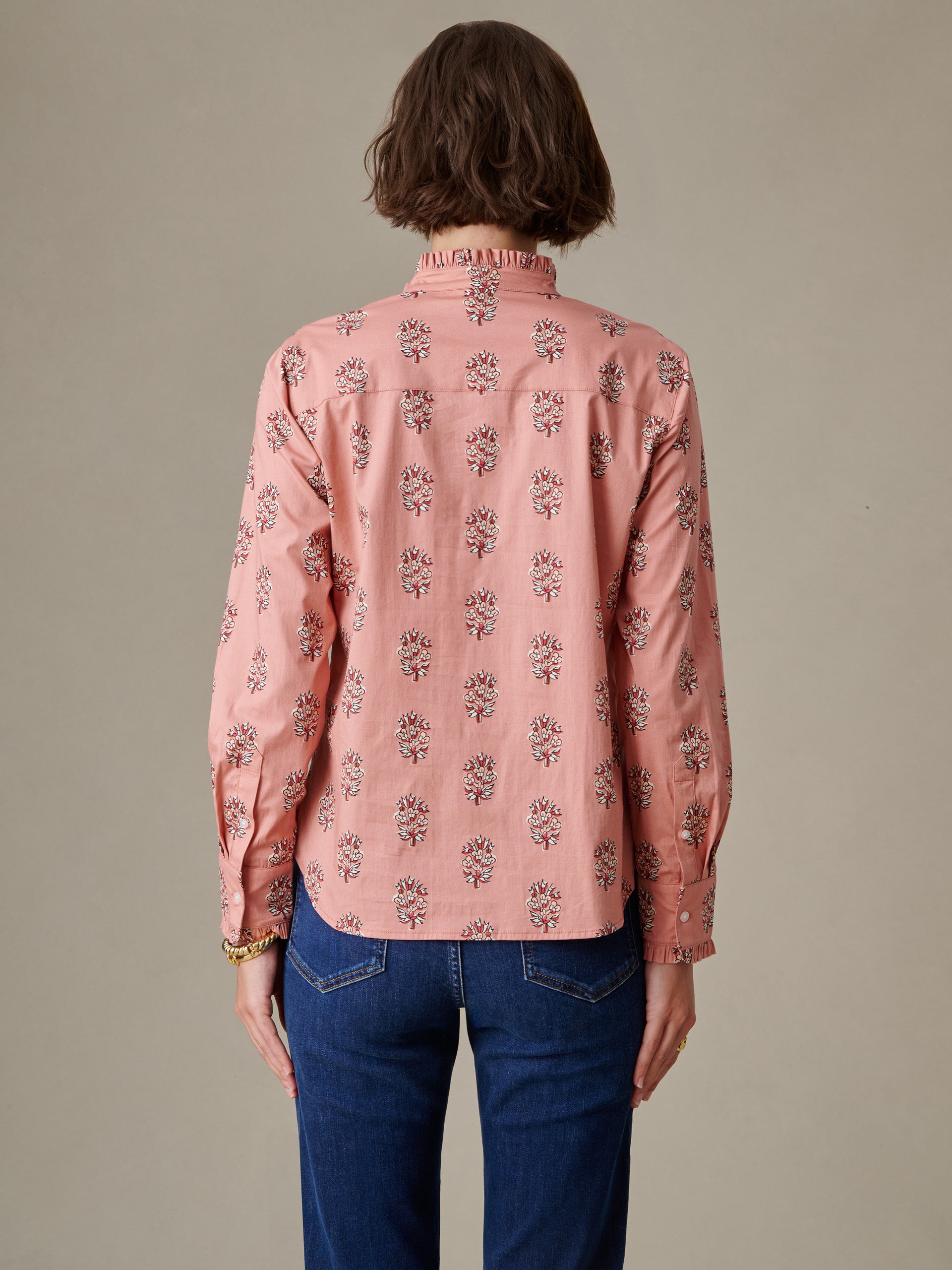 Woman seen from behind wearing the Tess Ruffle Collar Shirt in Heritage Bloom by J.McLaughlin, featuring a soft pink floral pattern and ruffled collar detail paired with blue jeans.