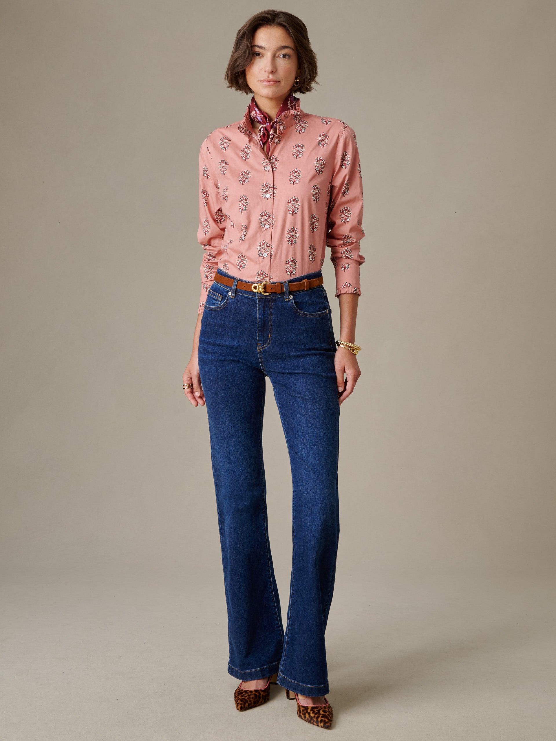 Woman wearing a pink Tess Ruffle Collar Shirt in Heritage Bloom by J.McLaughlin paired with high-waisted blue jeans, accessorized with a brown belt and leopard print heels.