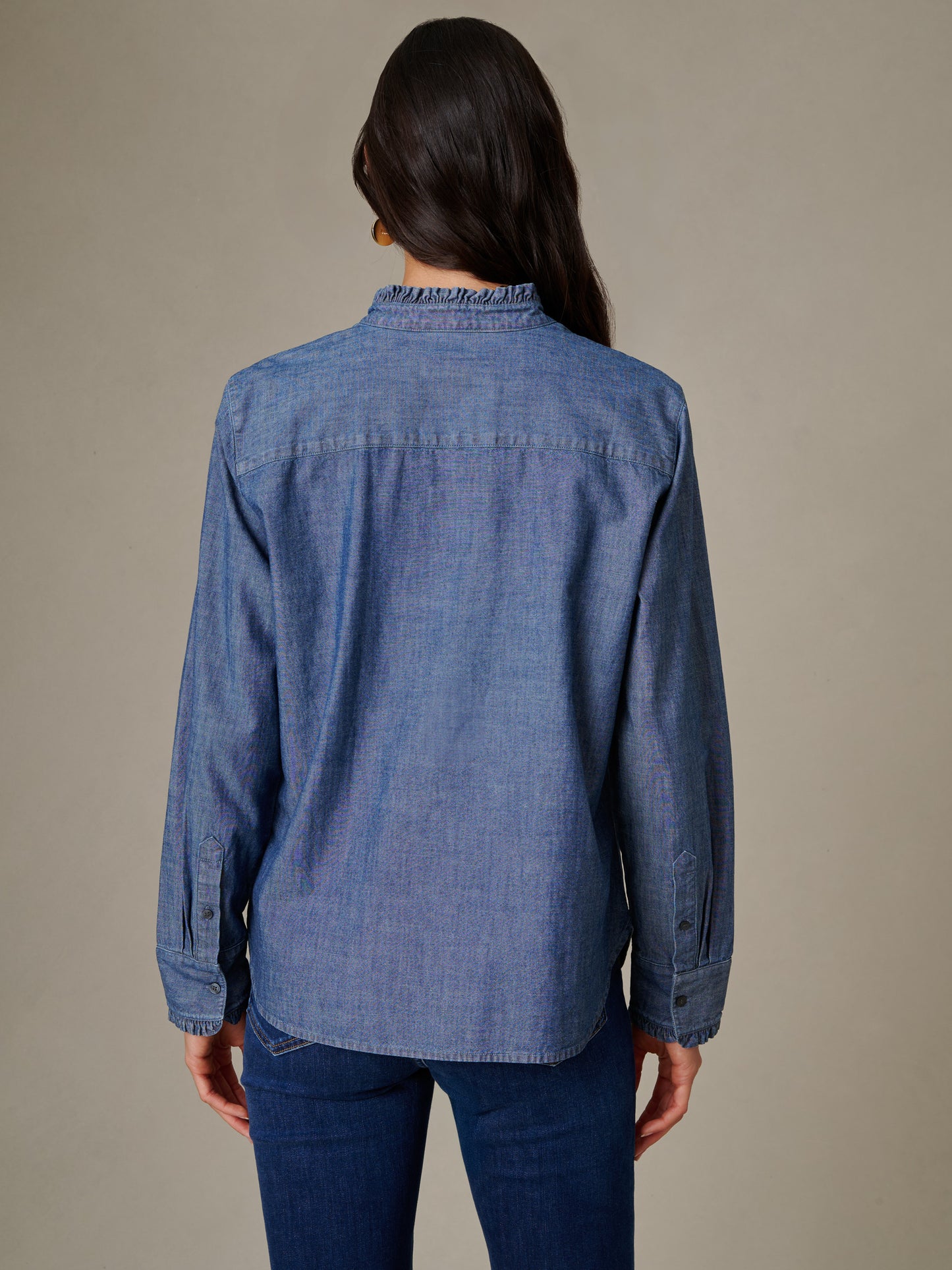Woman wearing a J.McLaughlin Tess Ruffle Collar Chambray Shirt, shown from the back, highlighting the classic chambray fabric and ruffle collar detail for an effortlessly stylish look.
