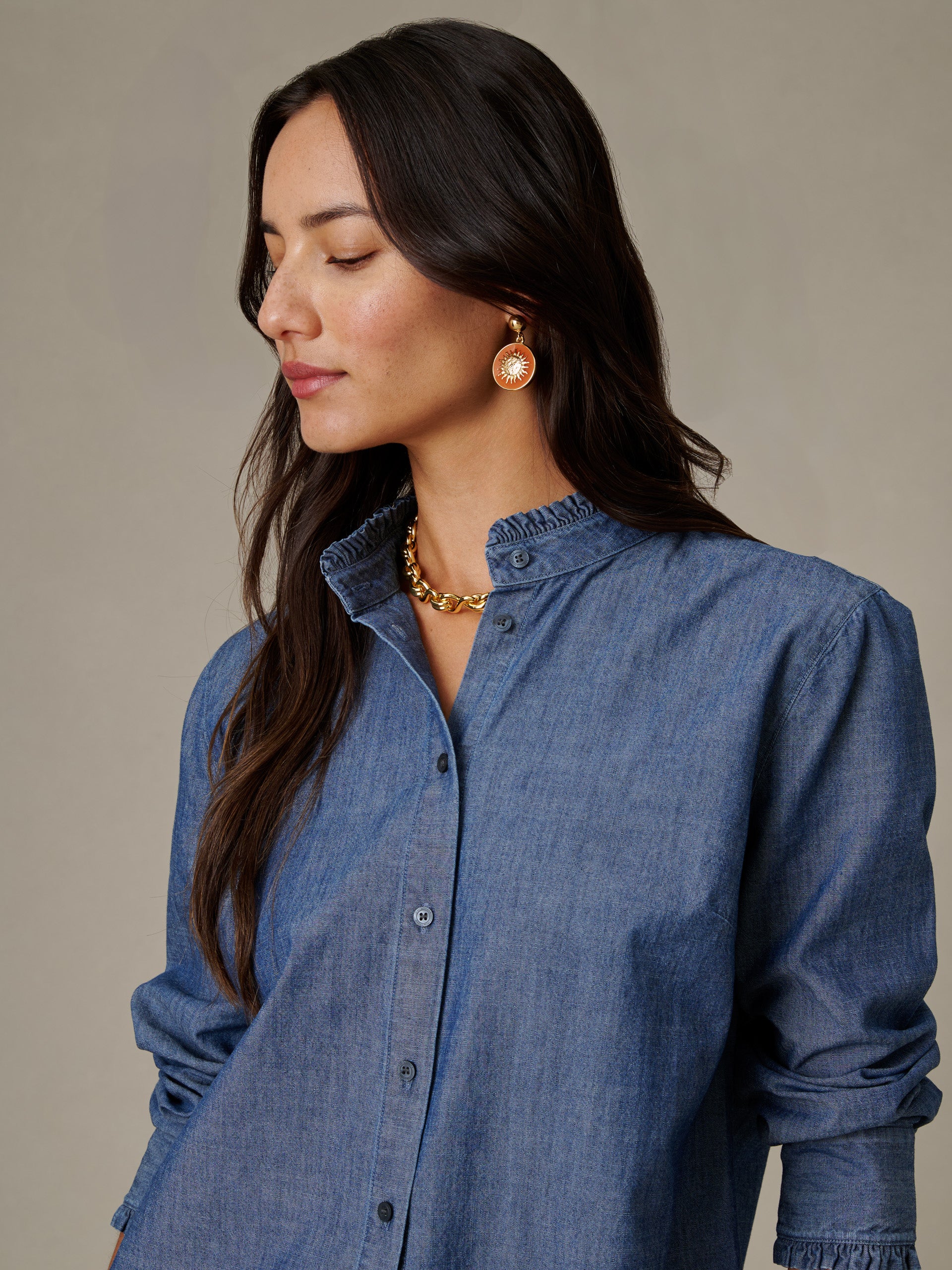 Woman wearing a J.McLaughlin Tess Ruffle Collar Chambray Shirt in soft blue, styled with gold earrings and necklace, showcasing timeless and effortlessly stylish design.