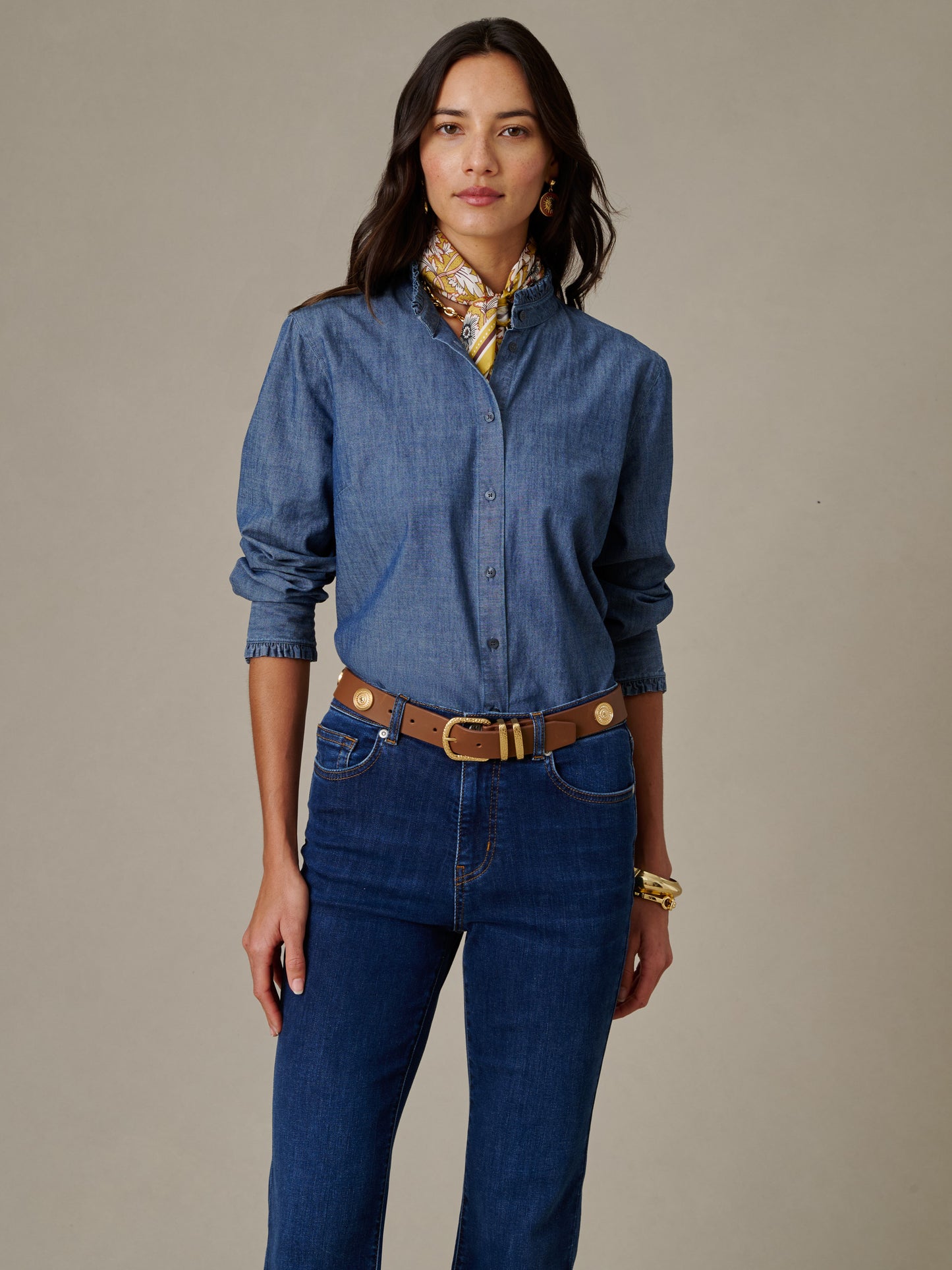 Woman wearing a Tess Ruffle Collar Chambray Shirt from J.McLaughlin paired with dark jeans, a brown belt, gold jewelry, and a patterned silk scarf, showcasing timeless style.
