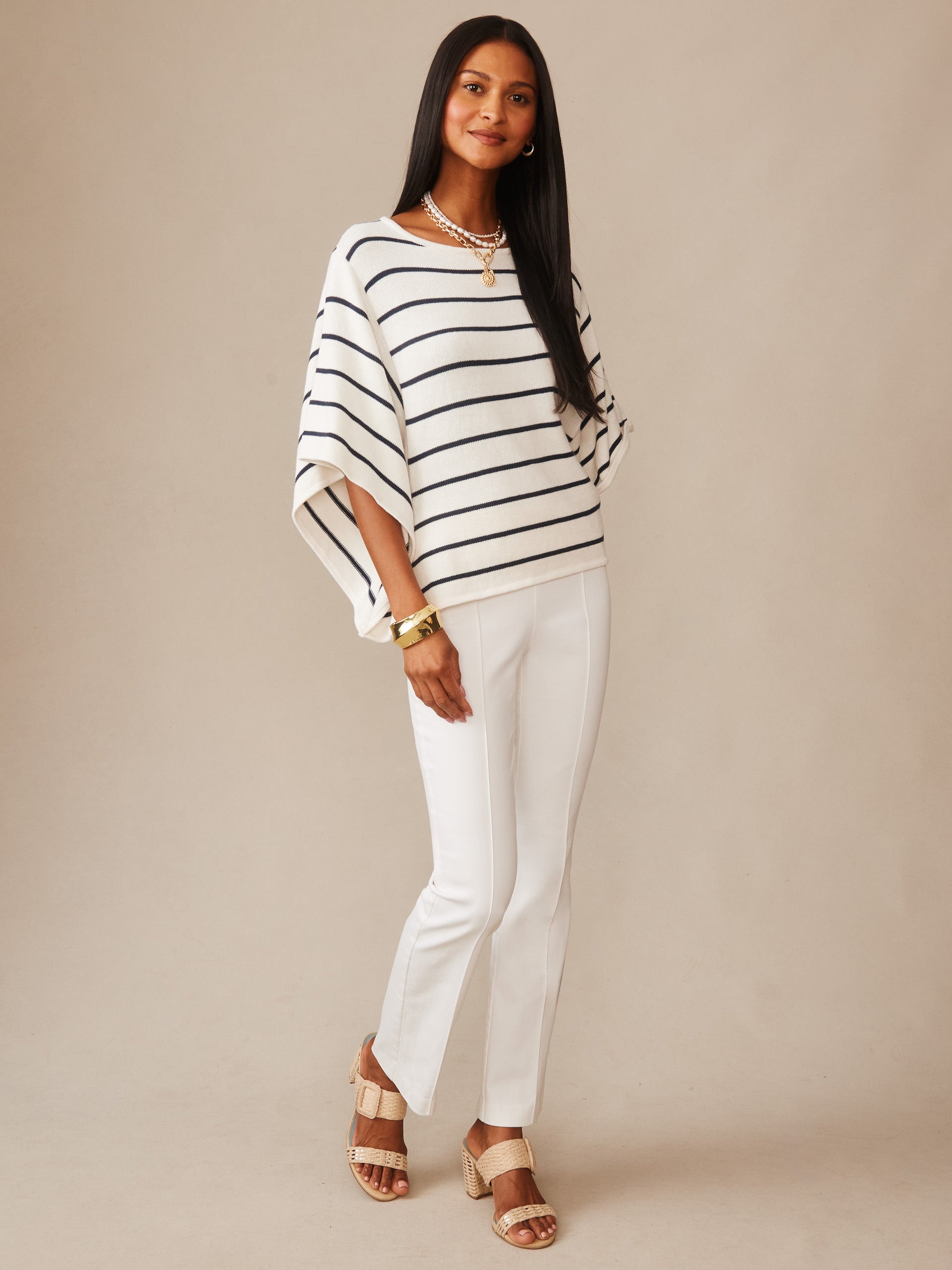 Woman wearing Thea Sweater in Stripe by J.McLaughlin, styled with white pants and beige sandals, embodying effortlessly stylish, enduring designs and a legacy of timeless fashion.