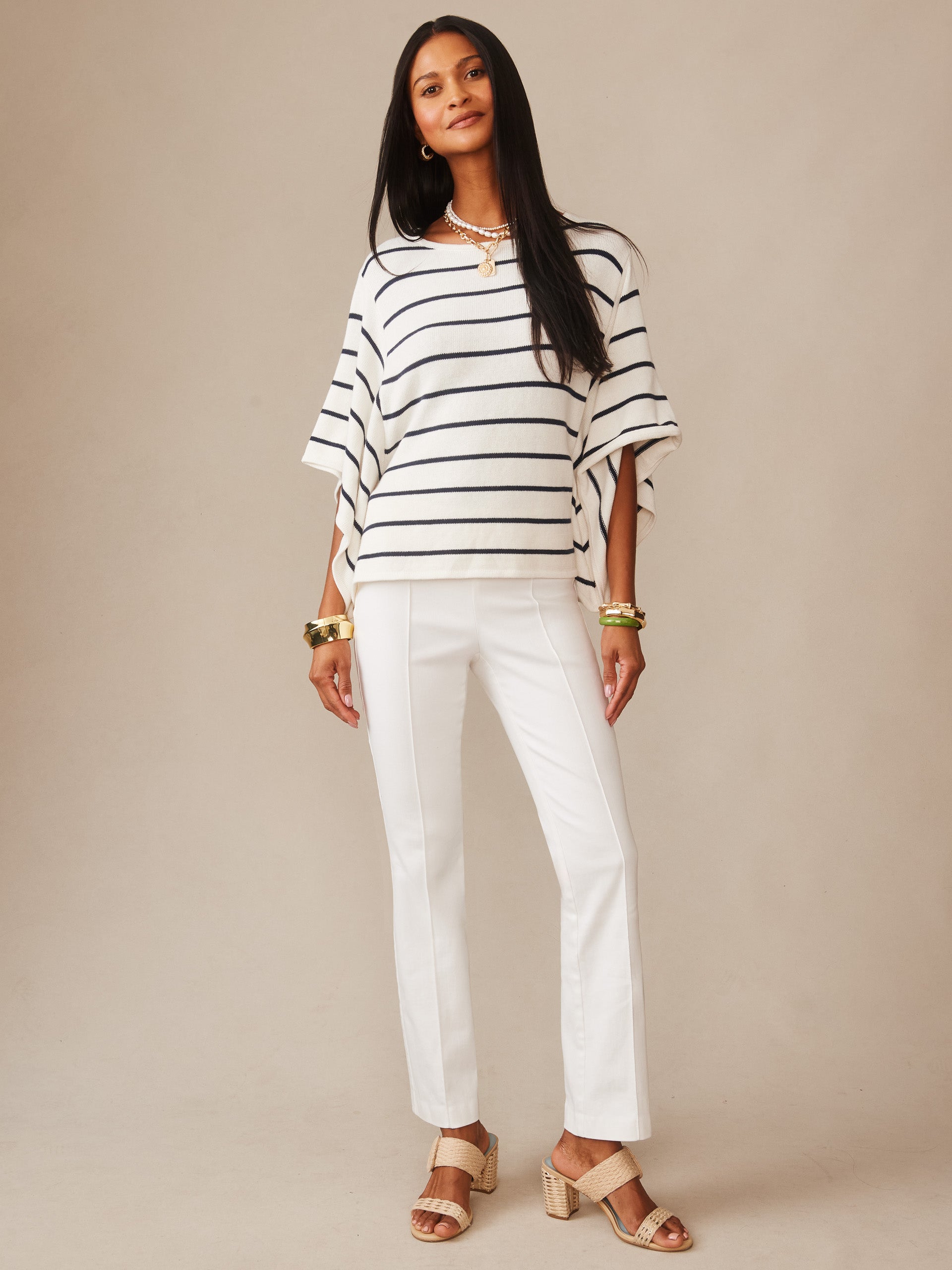 Woman wearing Thea Sweater in Stripe by J.McLaughlin, showcasing a classic striped white and navy sweater paired with white pants and sandals, embodying effortlessly stylish, enduring designs.