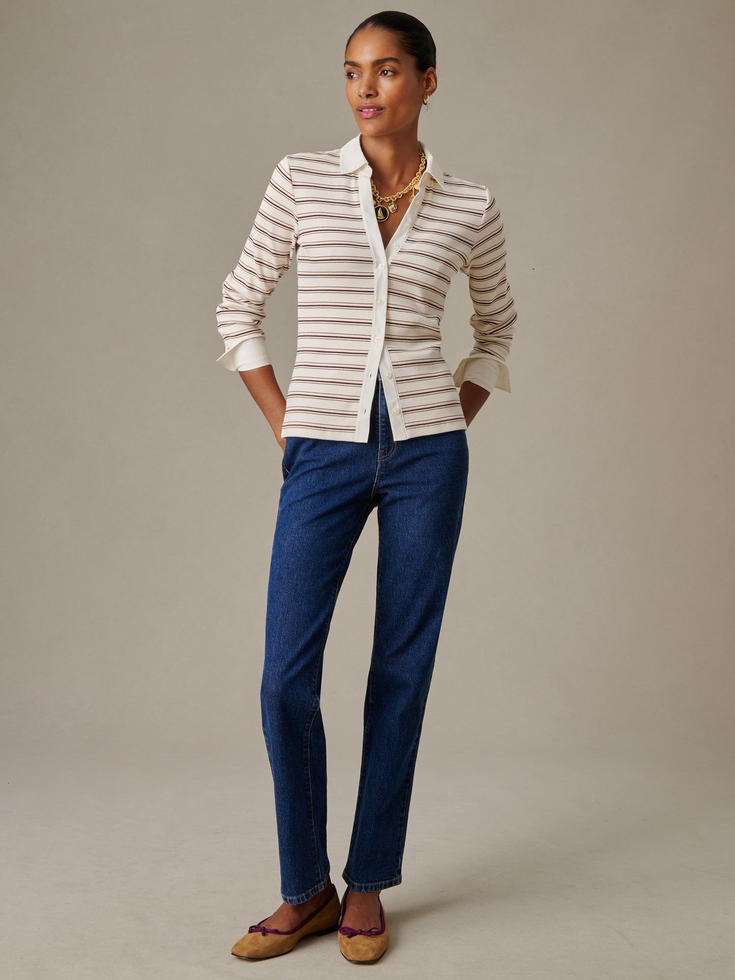 A model wearing the Theodora Shirt in Stripe by J.McLaughlin, styled with blue jeans and layered gold necklaces, showcasing effortlessly stylish, enduring designs.