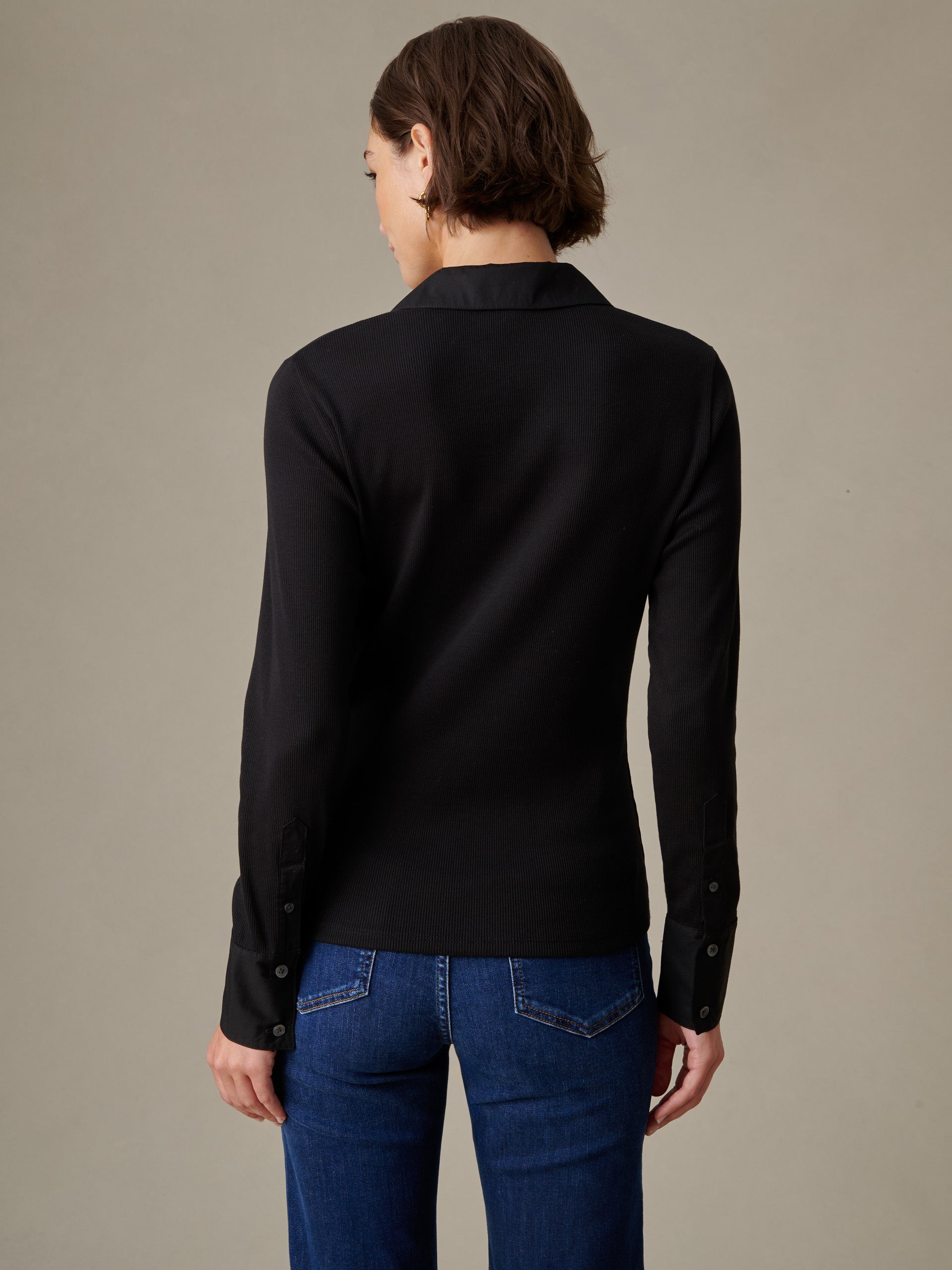 Woman wearing a black long-sleeve Theodora Shirt by J.McLaughlin paired with blue jeans, showcasing a timeless, effortlessly stylish top with enduring design and impeccable craftsmanship.