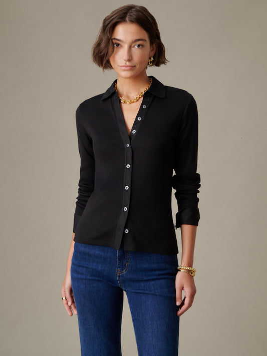 Woman wearing a black Theodora Shirt by J.McLaughlin paired with blue jeans, showcasing effortlessly stylish, enduring design with impeccable craftsmanship.