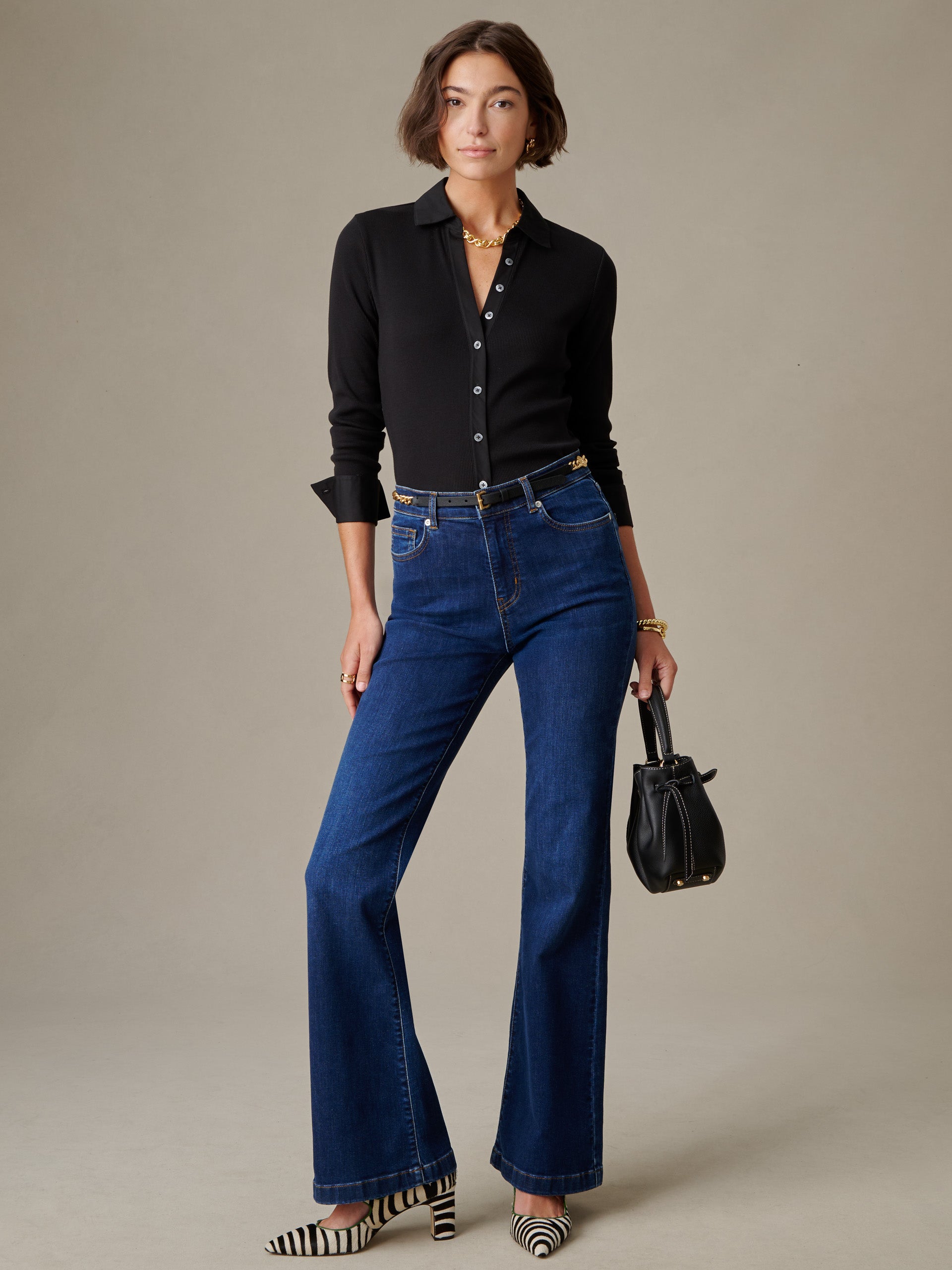 Woman wearing Theodora Shirt by J.McLaughlin, paired with dark blue jeans, holding a black handbag, showcasing effortlessly stylish and enduring designs from a legacy of timeless fashion.