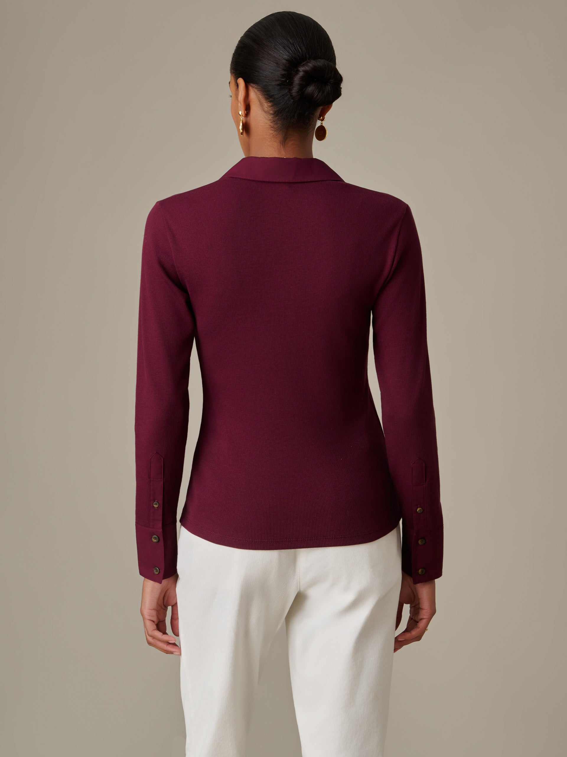 Woman seen from behind wearing J.McLaughlin Theodora Shirt in deep burgundy paired with white pants, showcasing timeless style and impeccable craftsmanship.