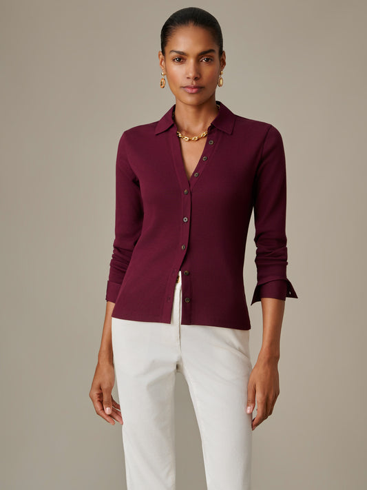 A model wearing the Theodora Shirt by J.McLaughlin in deep burgundy, styled with white pants and gold accessories, showcasing the brand’s effortlessly stylish and enduring design.