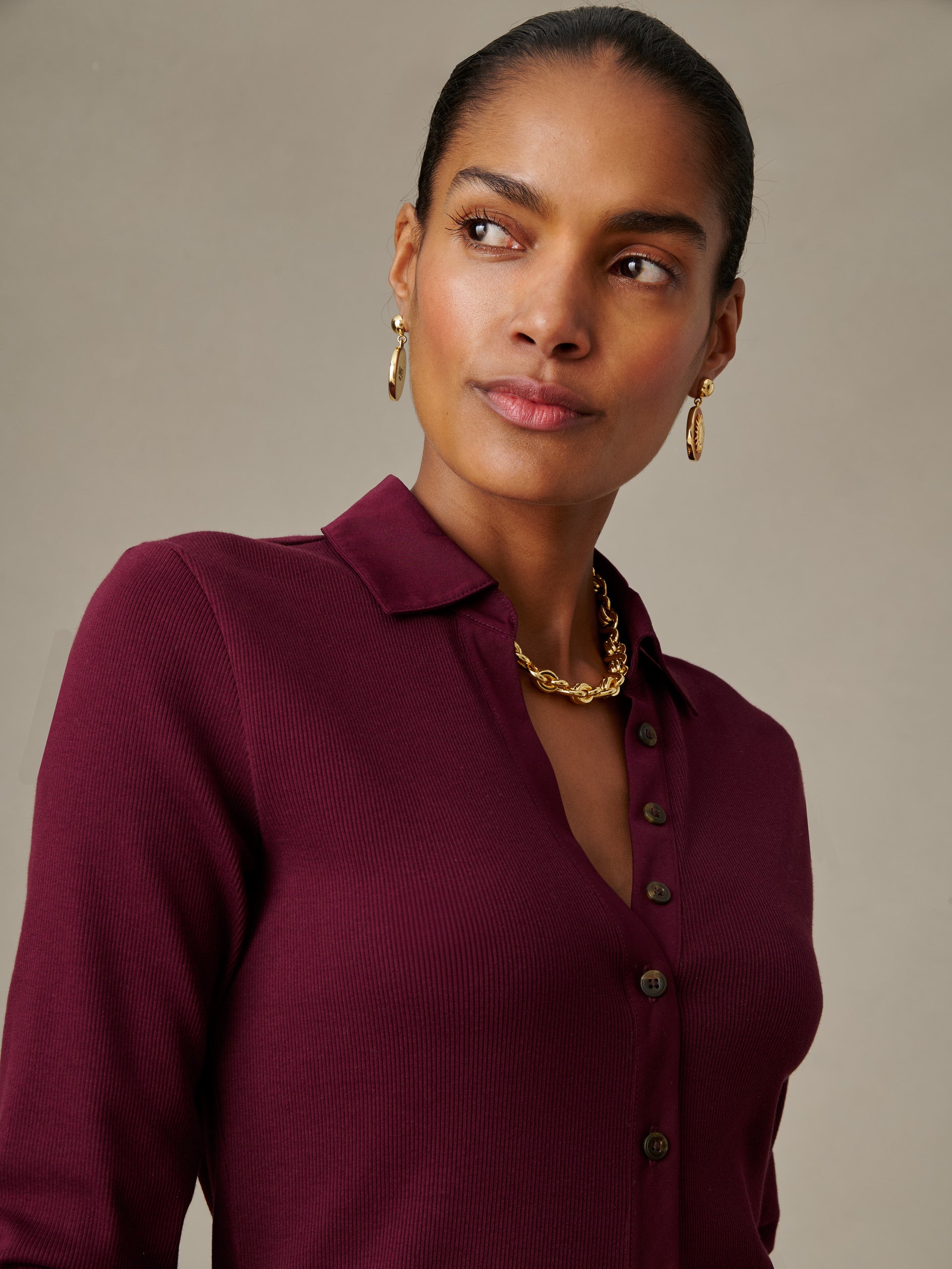 Woman wearing a burgundy Theodora Shirt by J.McLaughlin with a classic collar and button details, styled with gold earrings and a chain necklace.