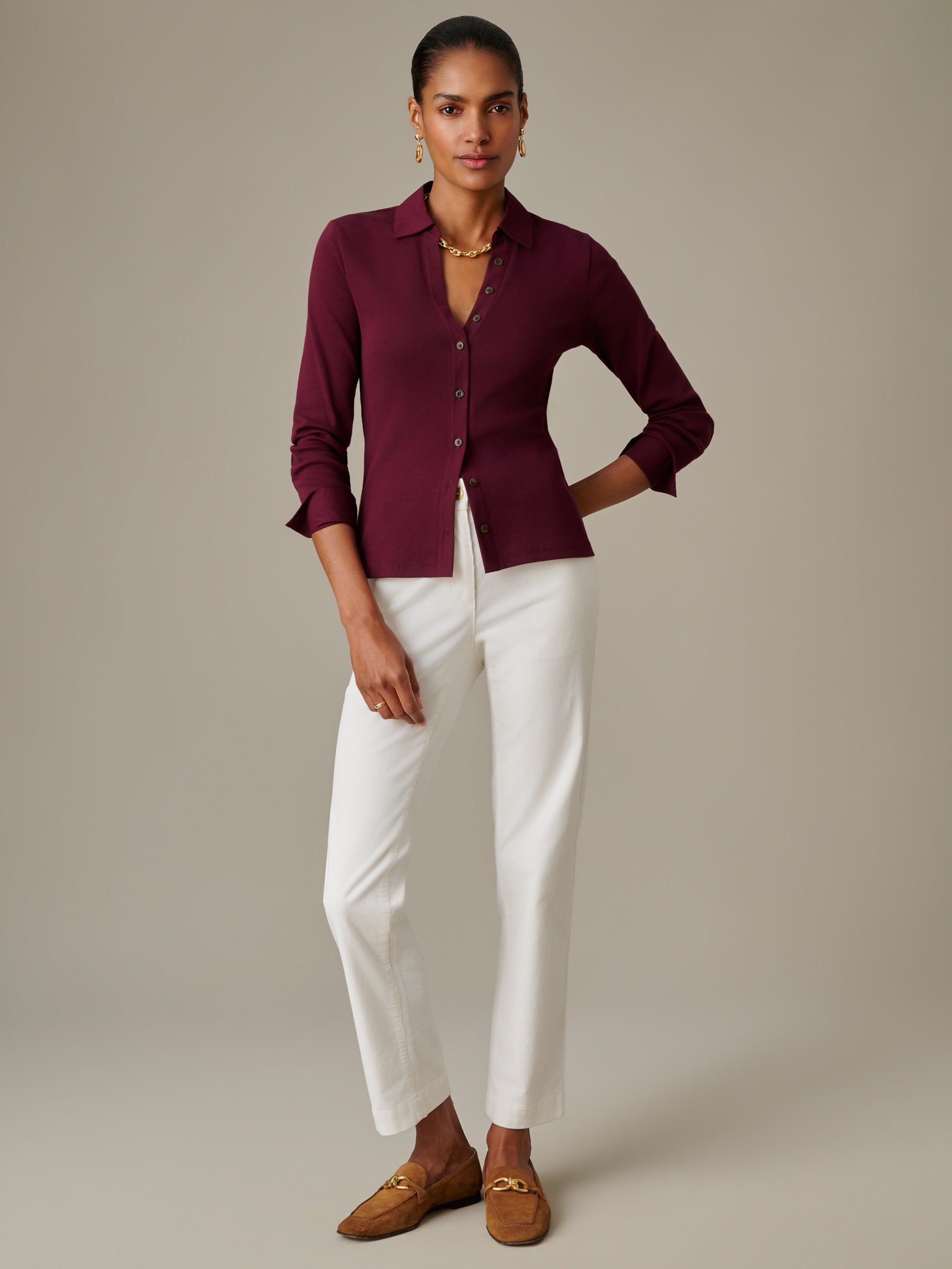 Model wearing Theodora Shirt by J.McLaughlin in a deep berry tone, paired with white pants and brown loafers, showcasing effortlessly stylish, enduring designs.