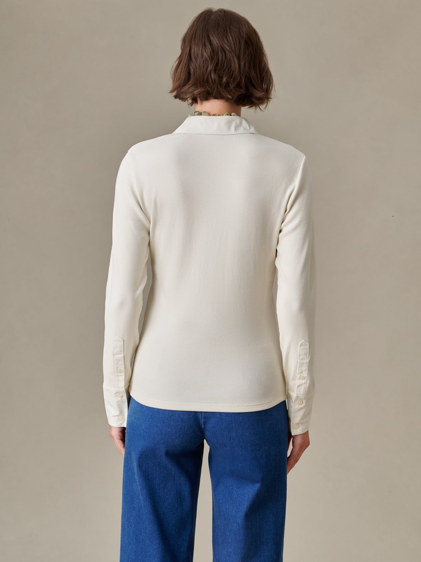 Back view of a woman wearing a cream long-sleeve Theodora Shirt paired with blue jeans, showcasing J.McLaughlin’s effortlessly stylish and enduring designs.