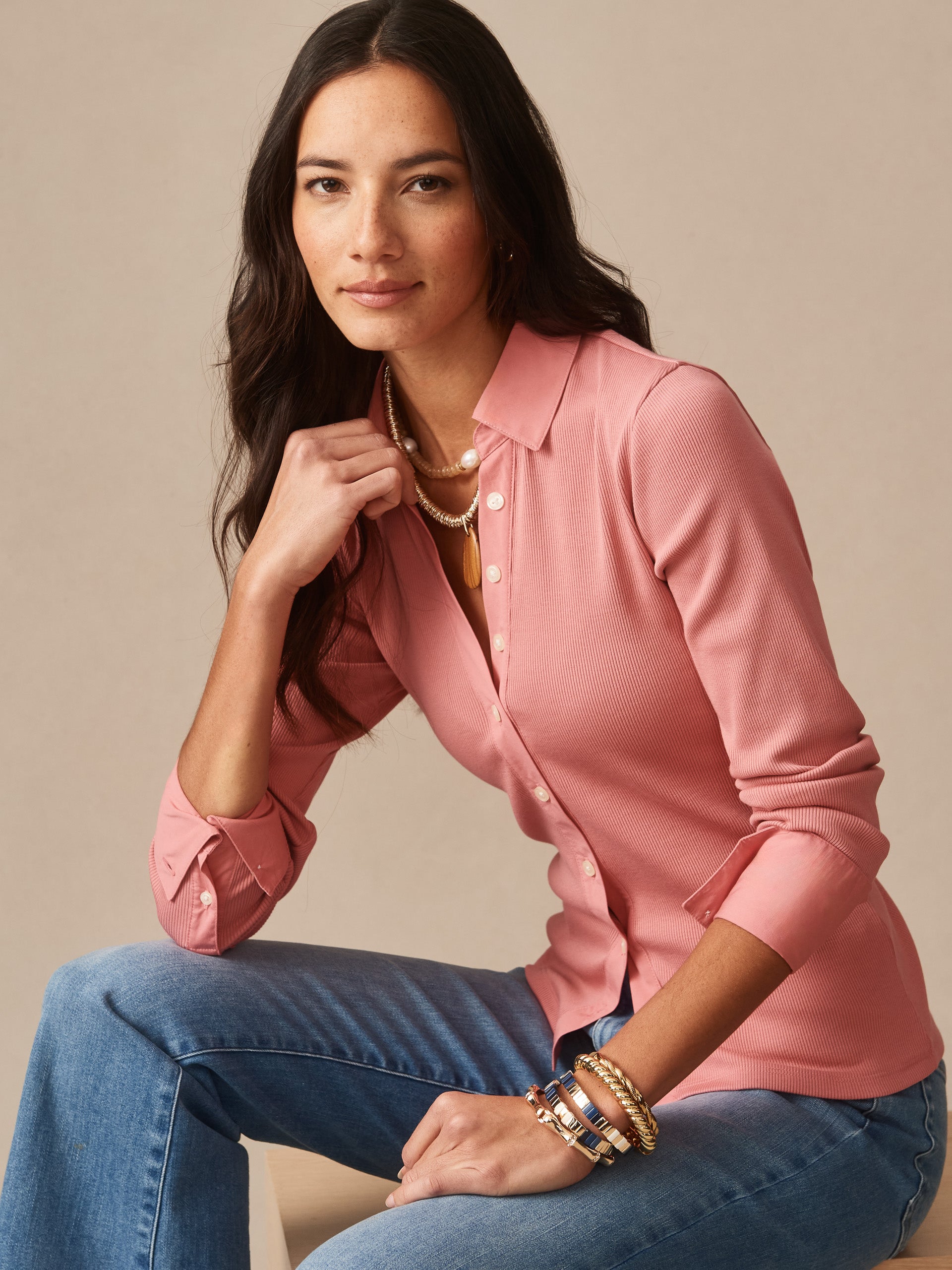 Woman wearing mauve pink Theodora Shirt by J.McLaughlin, styled with jeans and gold bracelets, showcasing effortlessly stylish, enduring designs and innovative fabrics.