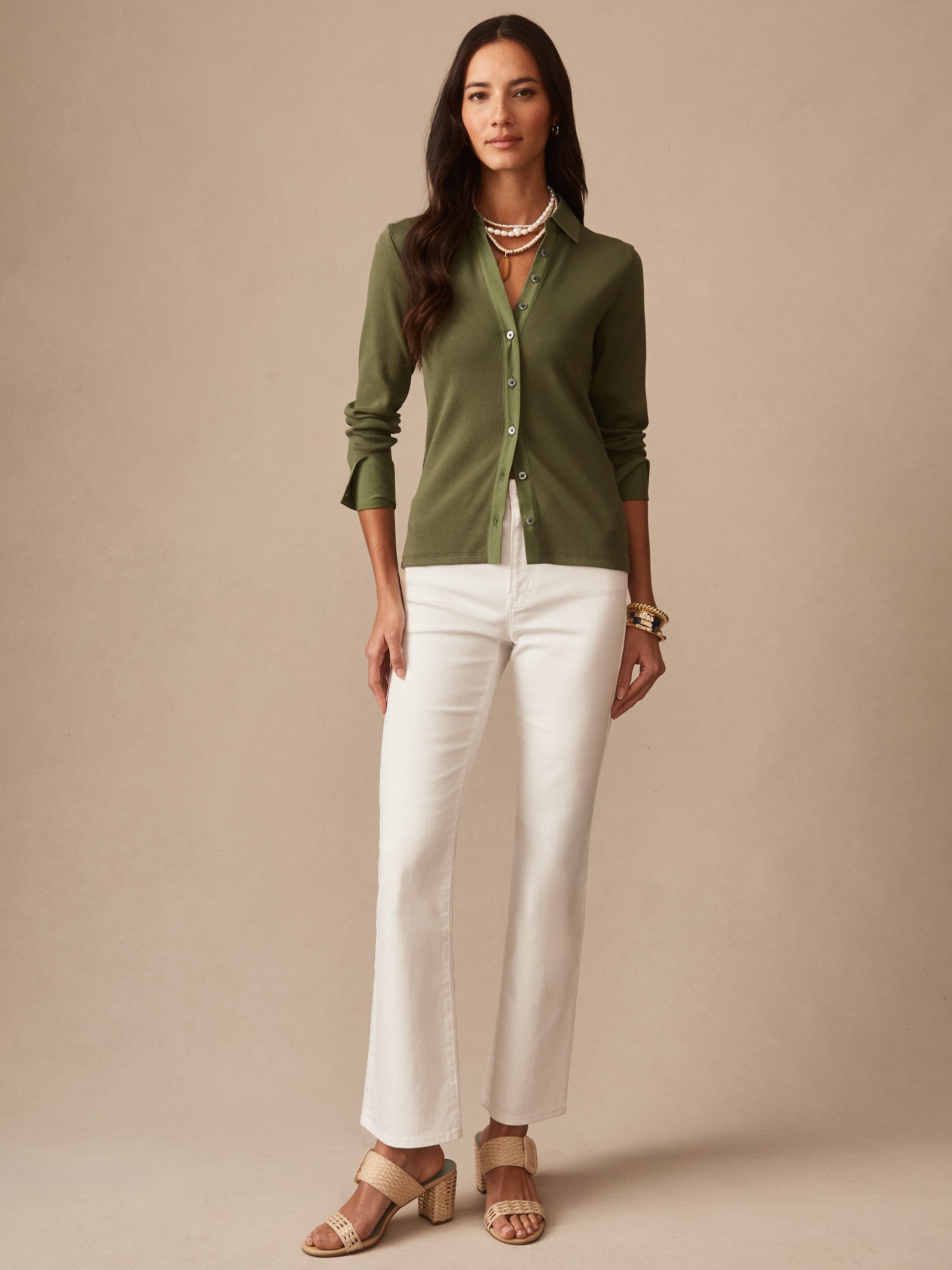 Woman wearing Theodora Shirt in moss green by J.McLaughlin paired with white pants and layered necklaces, showcasing effortlessly stylish pieces with enduring designs and innovative fabrics.