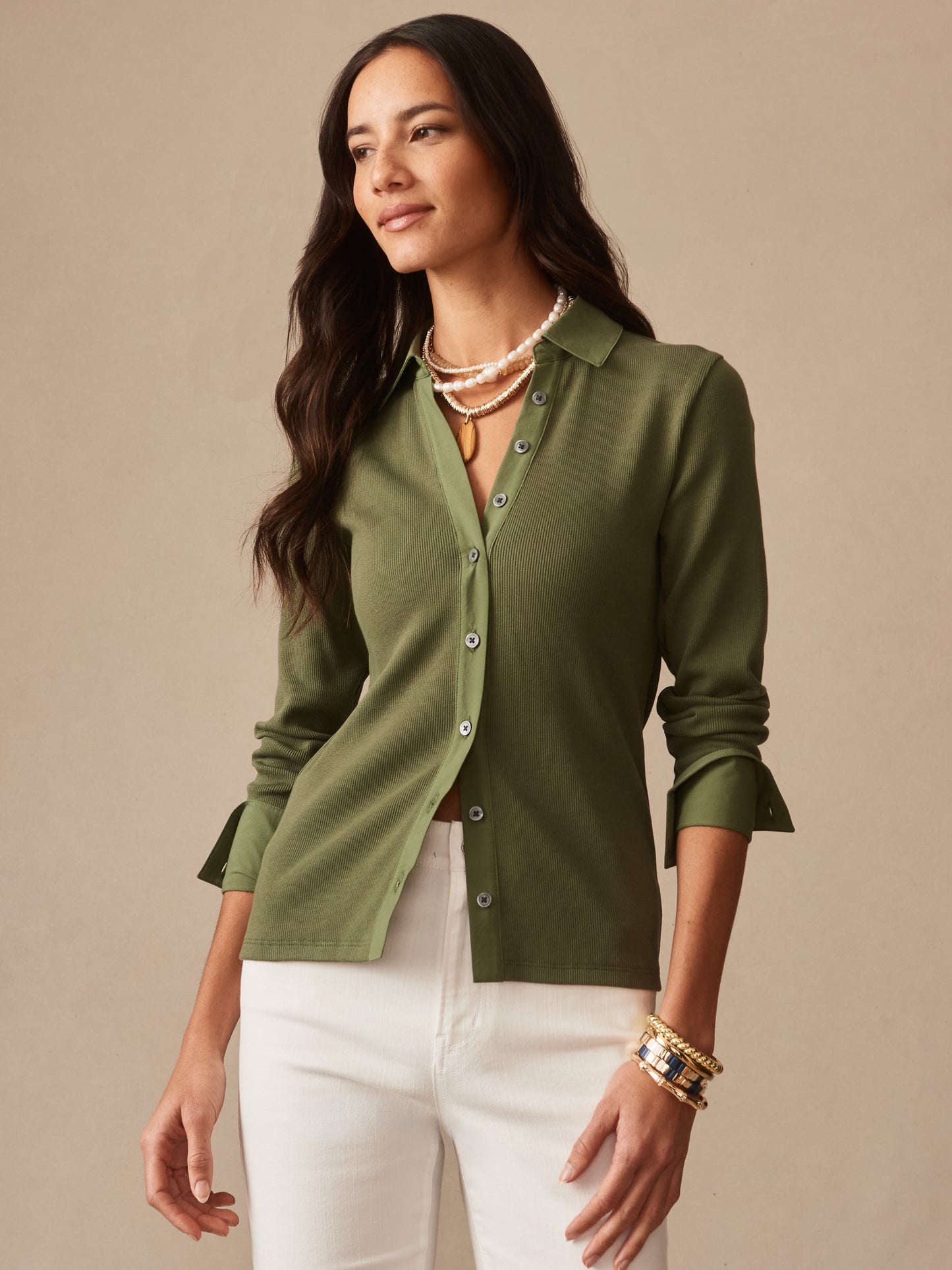 A woman wearing the Theodora Shirt in moss green by J.McLaughlin, styled with layered necklaces and bracelets, showcasing effortlessly stylish and enduring designs.