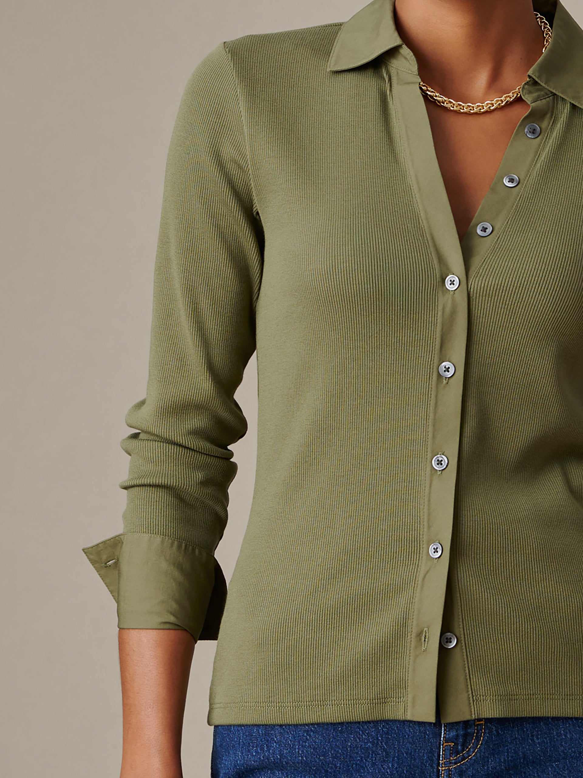 Close-up of a person wearing the olive green Theodora Shirt by J.McLaughlin, featuring a ribbed texture, button-down front, and a gold chain necklace, showcasing effortless style.