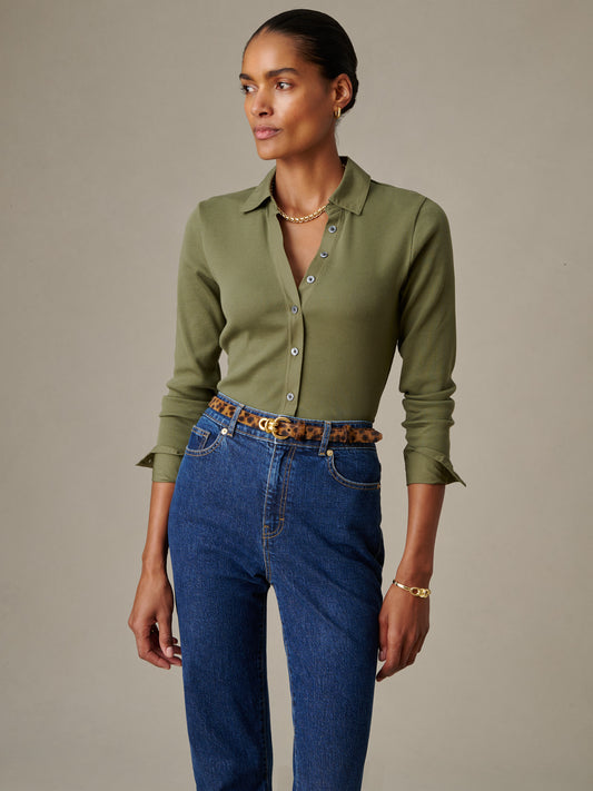 A model wearing the olive green Theodora Shirt by J.McLaughlin paired with high-waisted jeans and a leopard print belt, showcasing effortlessly stylish, enduring designs.