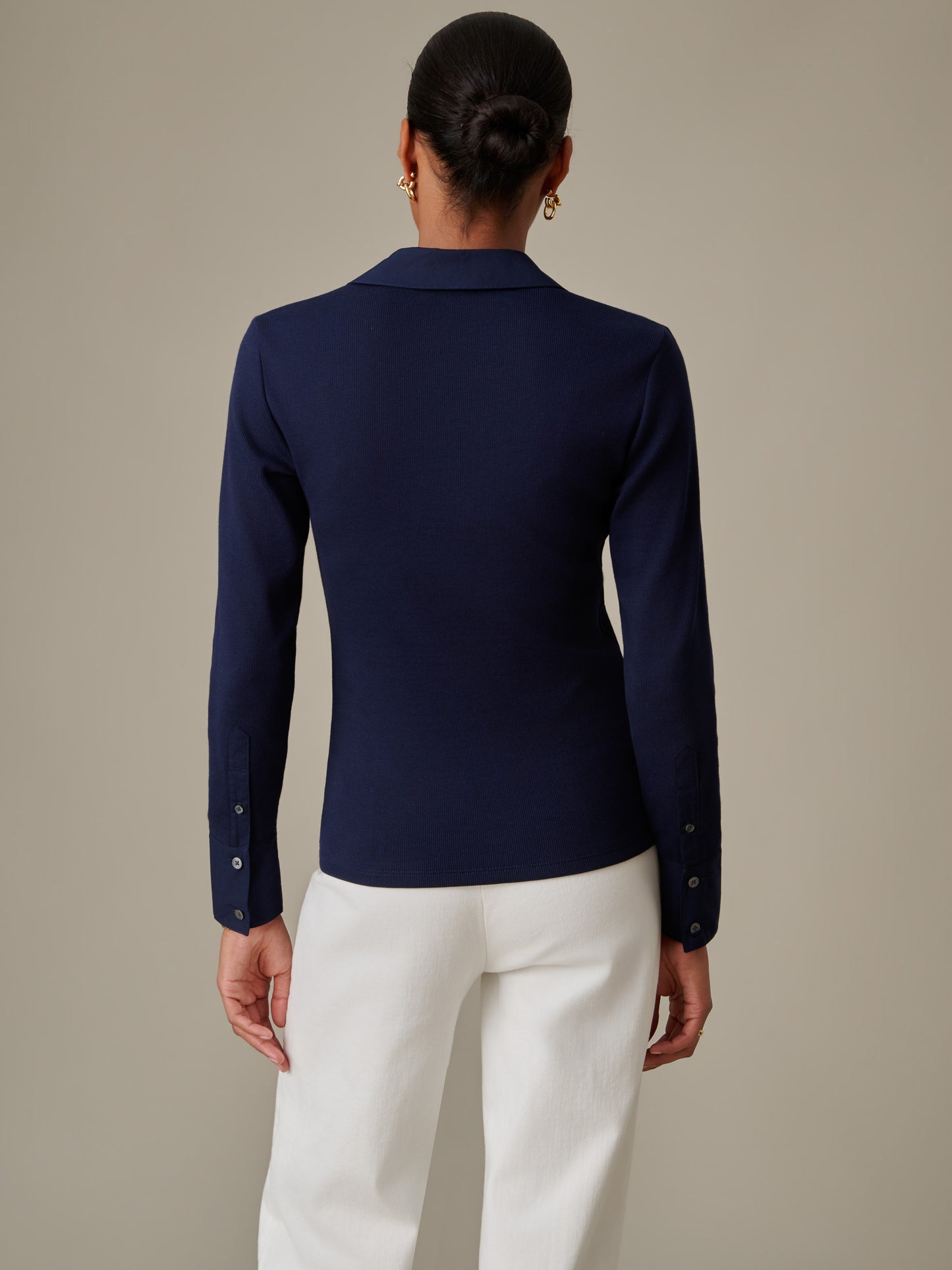 Woman wearing a navy blue Theodora Shirt by J.McLaughlin, paired with white pants, showcasing timeless, effortlessly stylish design with a tailored fit and long sleeves.