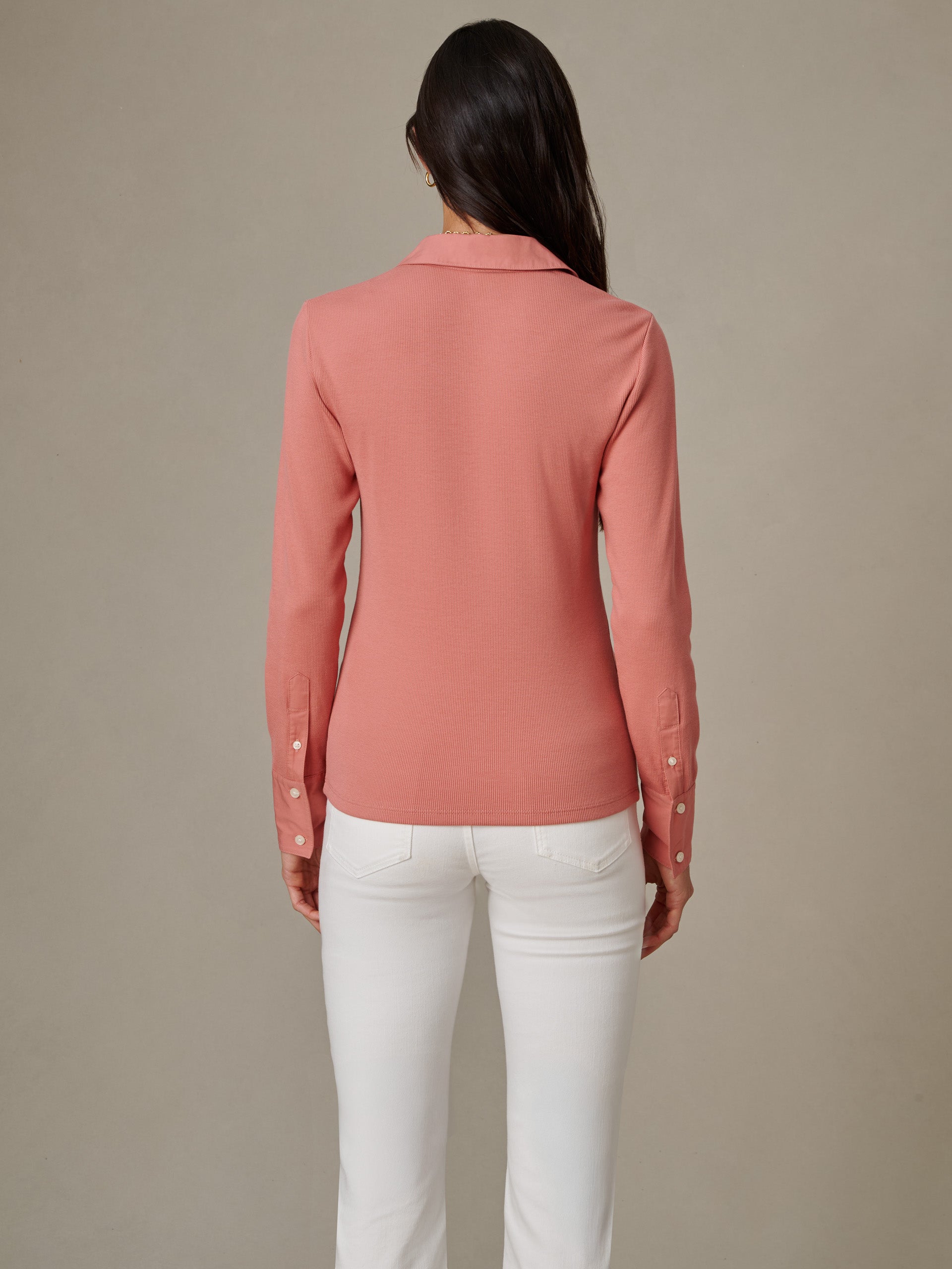 Woman wearing a long-sleeve Theodora Shirt in muted rose by J.McLaughlin, paired with white pants, showcasing timeless style and impeccable craftsmanship.