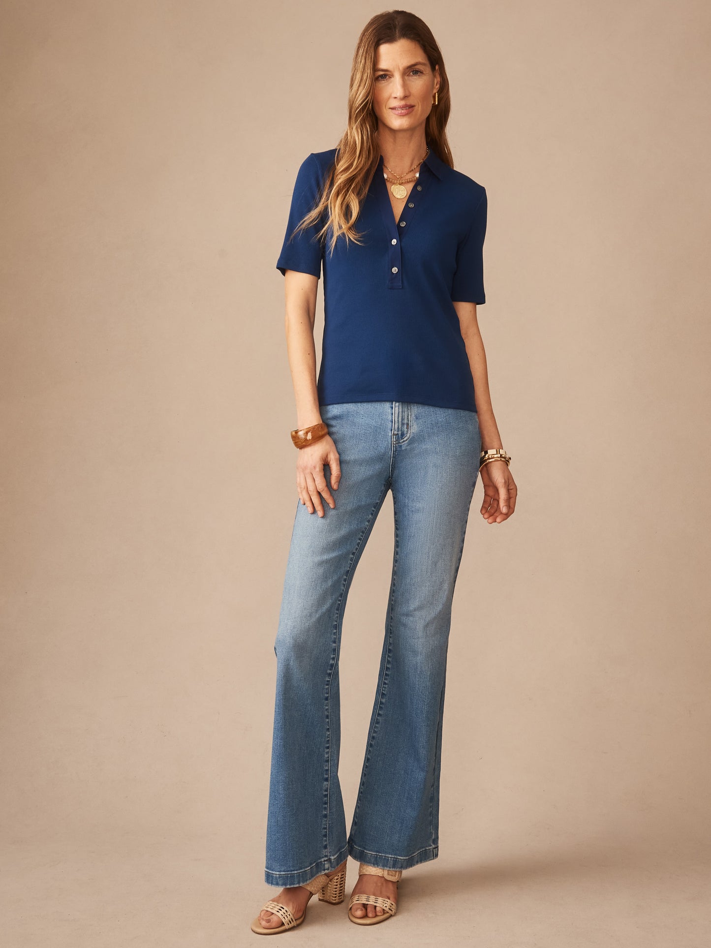 A model wearing the Theodora Short Sleeve Shirt in nautical navy by J.McLaughlin, paired with light wash flared jeans and sandals, showcasing effortlessly stylish, enduring designs.