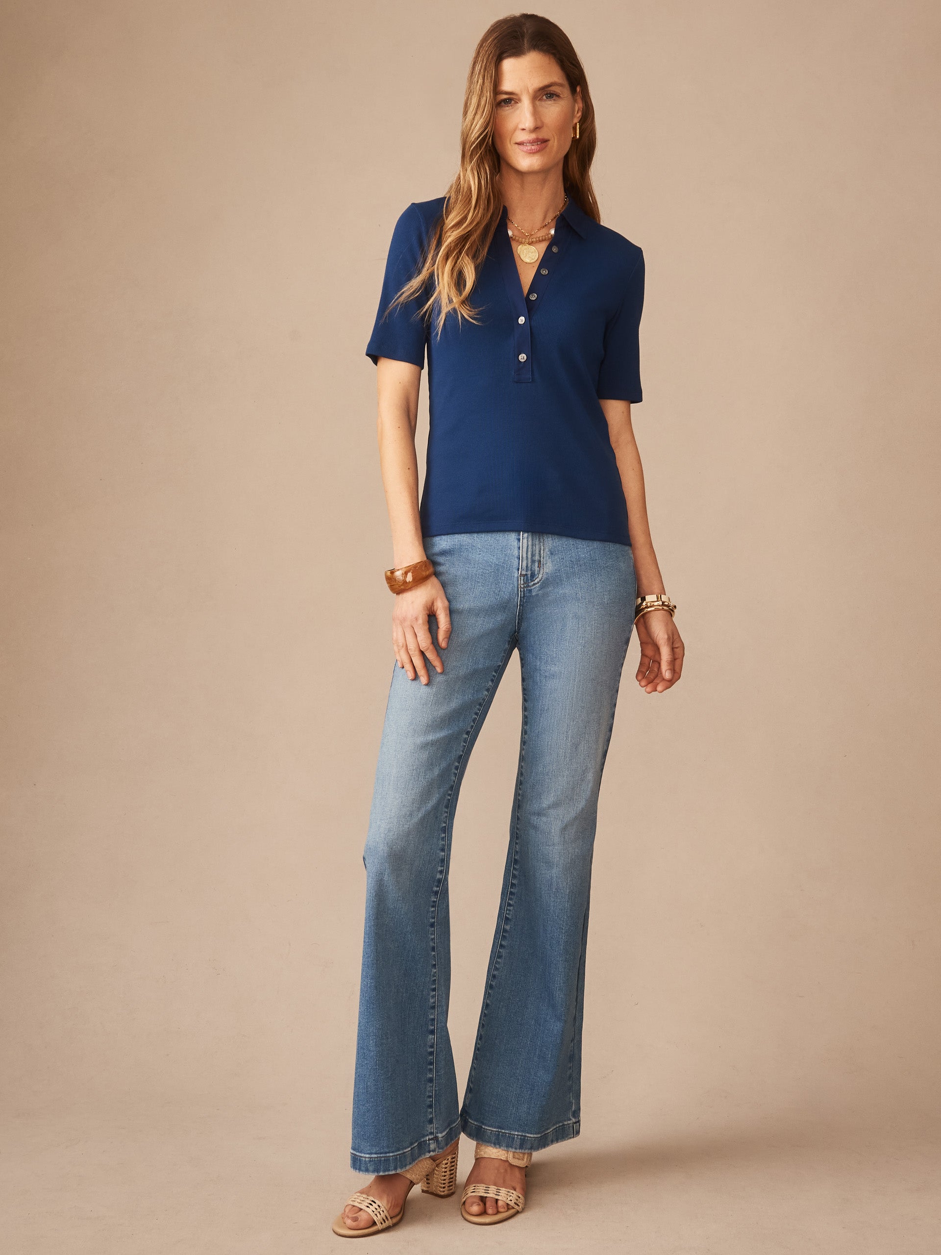 A model wearing the Theodora Short Sleeve Shirt in nautical navy by J.McLaughlin, paired with light wash flared jeans and sandals, showcasing effortlessly stylish, enduring designs.