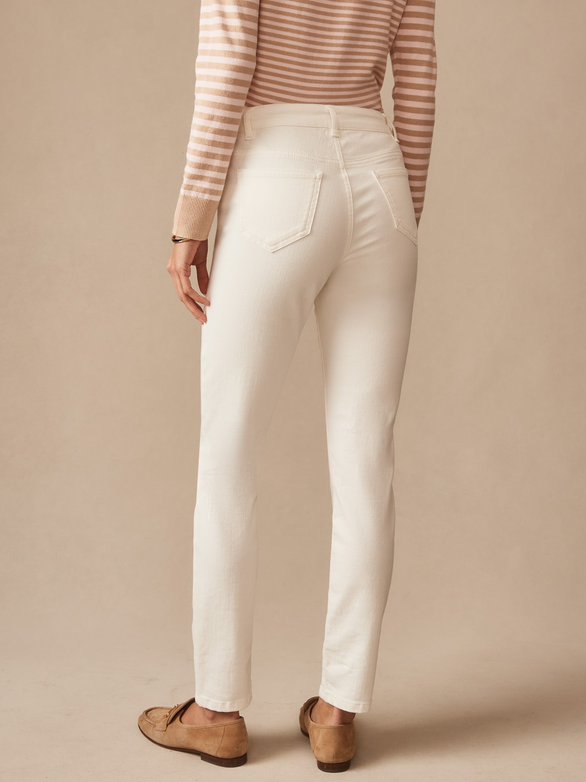 Back view of a person wearing white Watson Jeans by J.McLaughlin paired with a beige striped long-sleeve top and tan loafers, showcasing timeless style and quality craftsmanship.